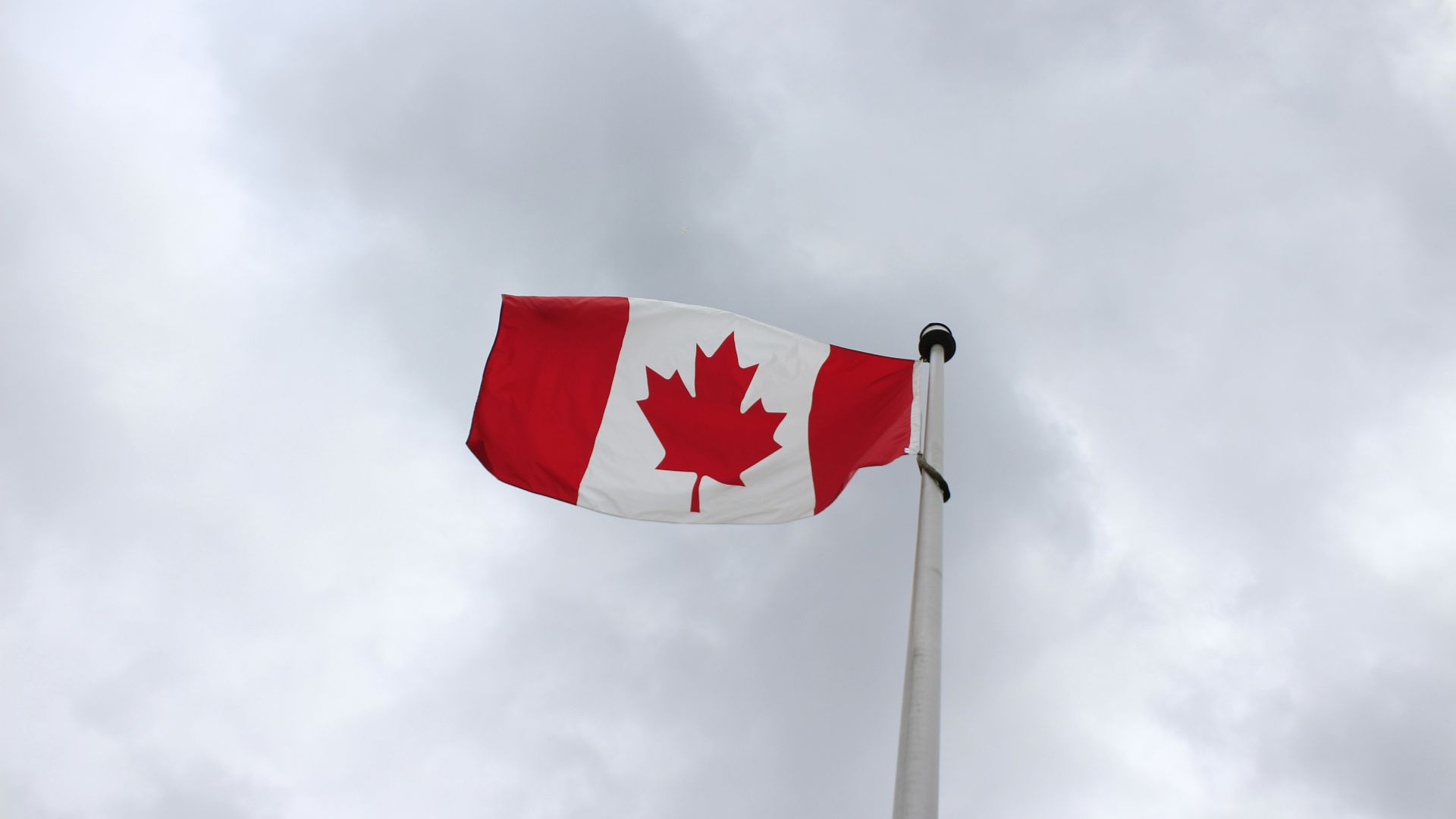a canadian flag flying in the wind on a cloudy day