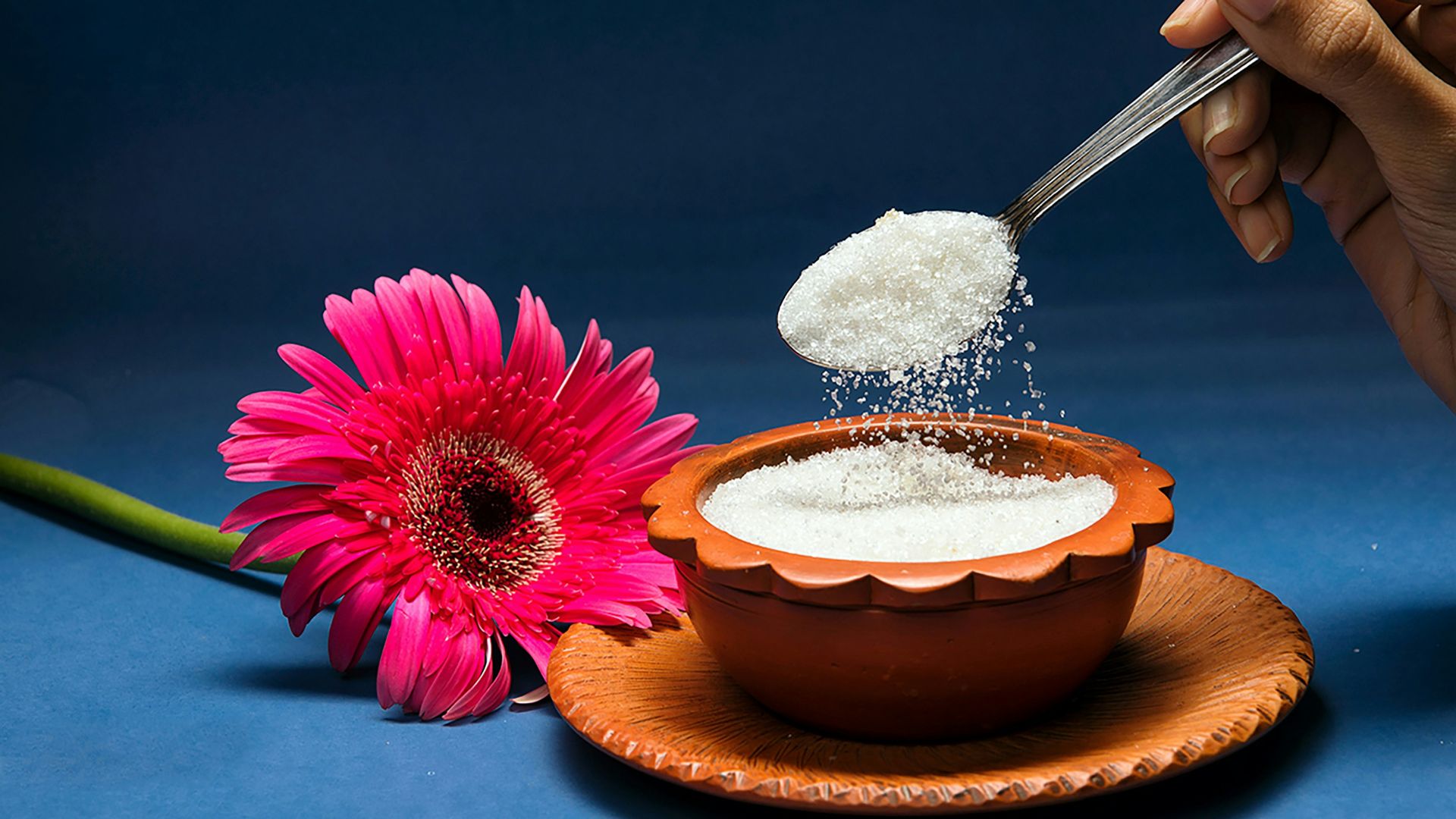 Spoon pouring sugar into a bowl with flower.