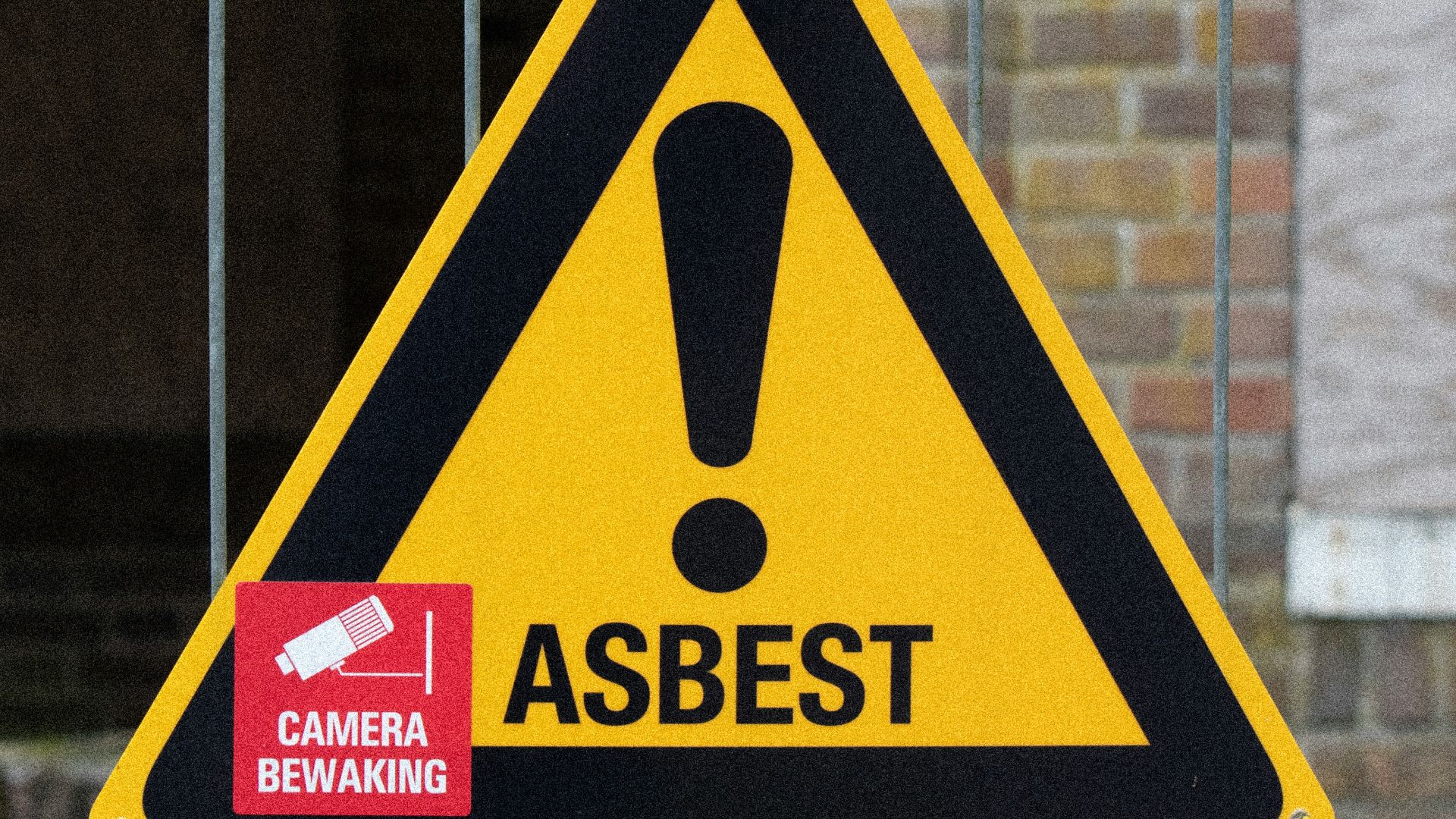 A yellow and black warning sign on a fence
