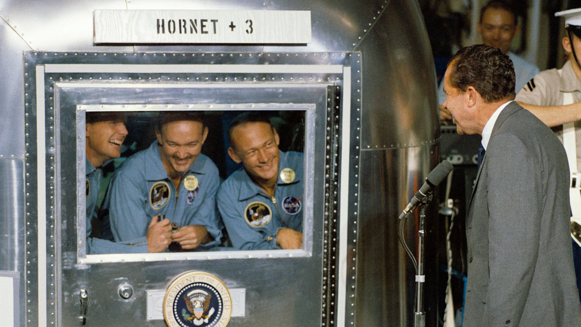 man in gray suit jacket in front of microphone with stand