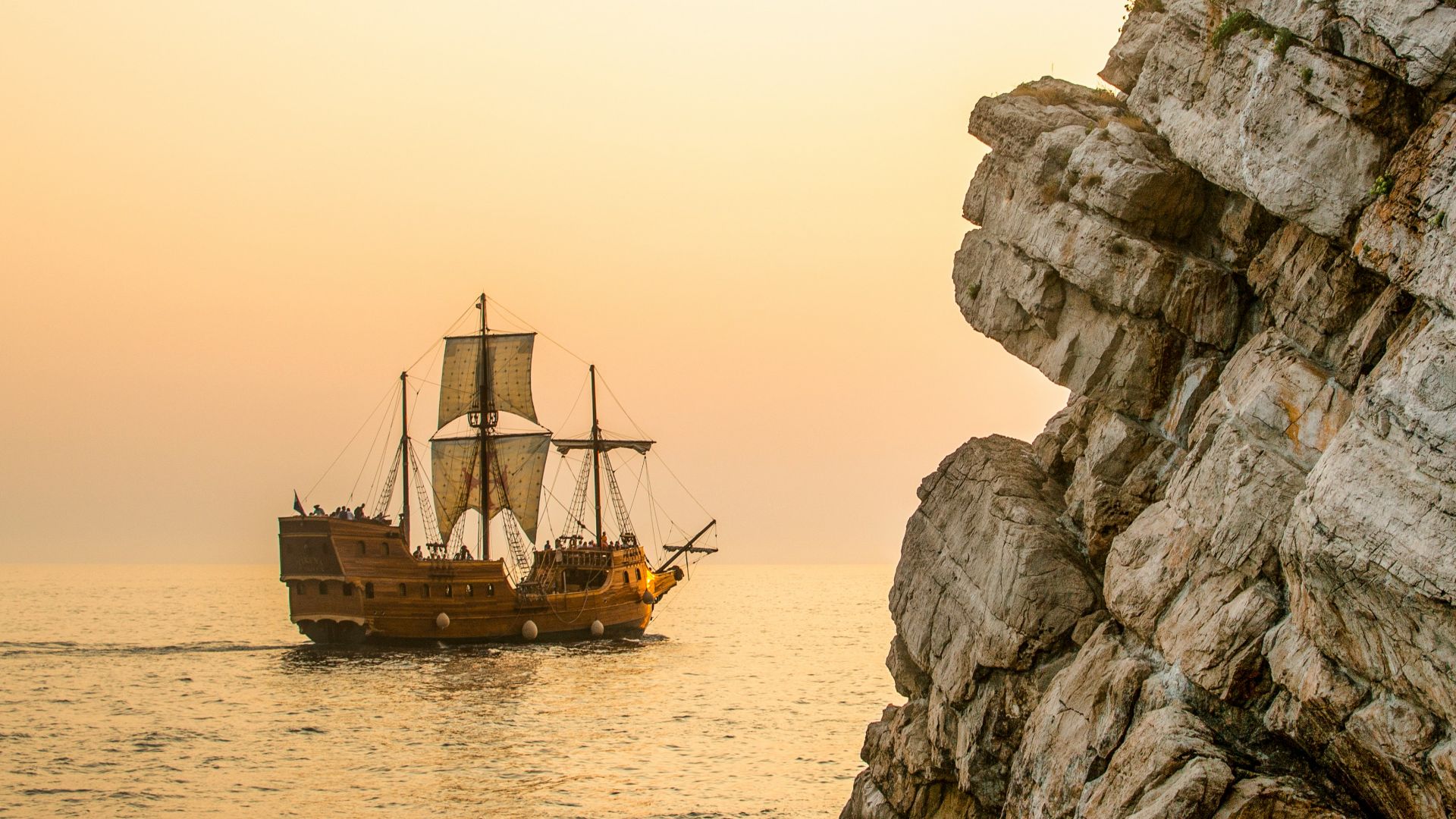 a boat sailing on the water near a rocky cliff