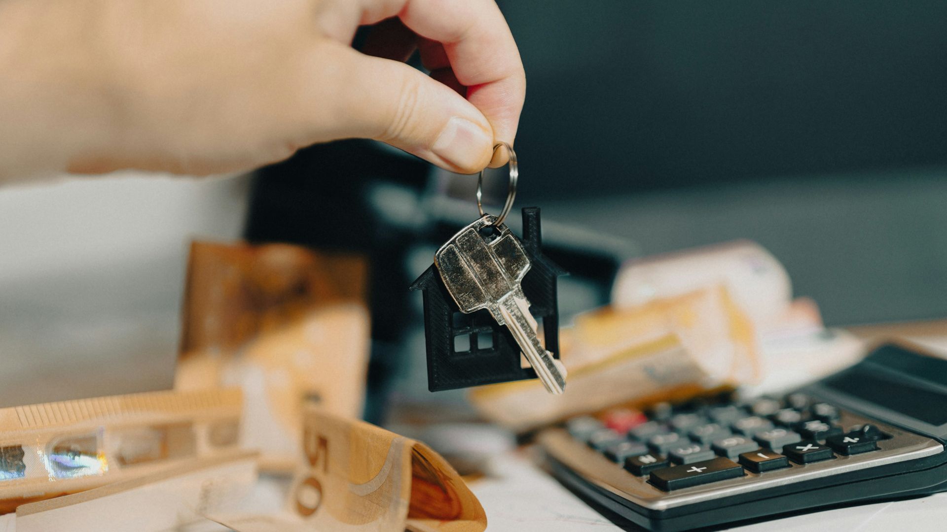 A person holding a house key in front of a calculator
