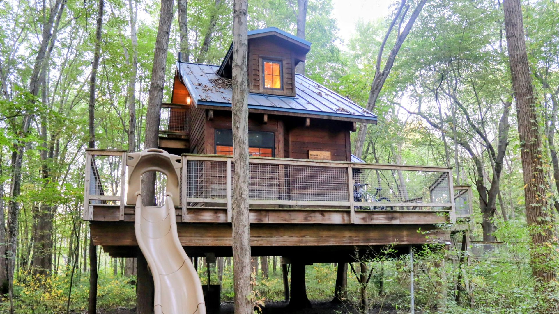 Wooden treehouse with slide in a forest setting.