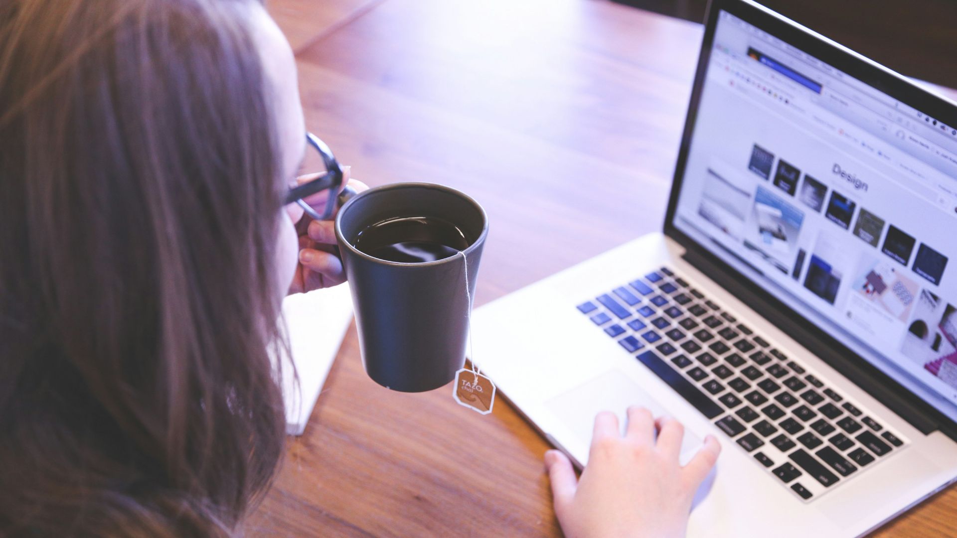 woman holding tea filled mug using MacBook