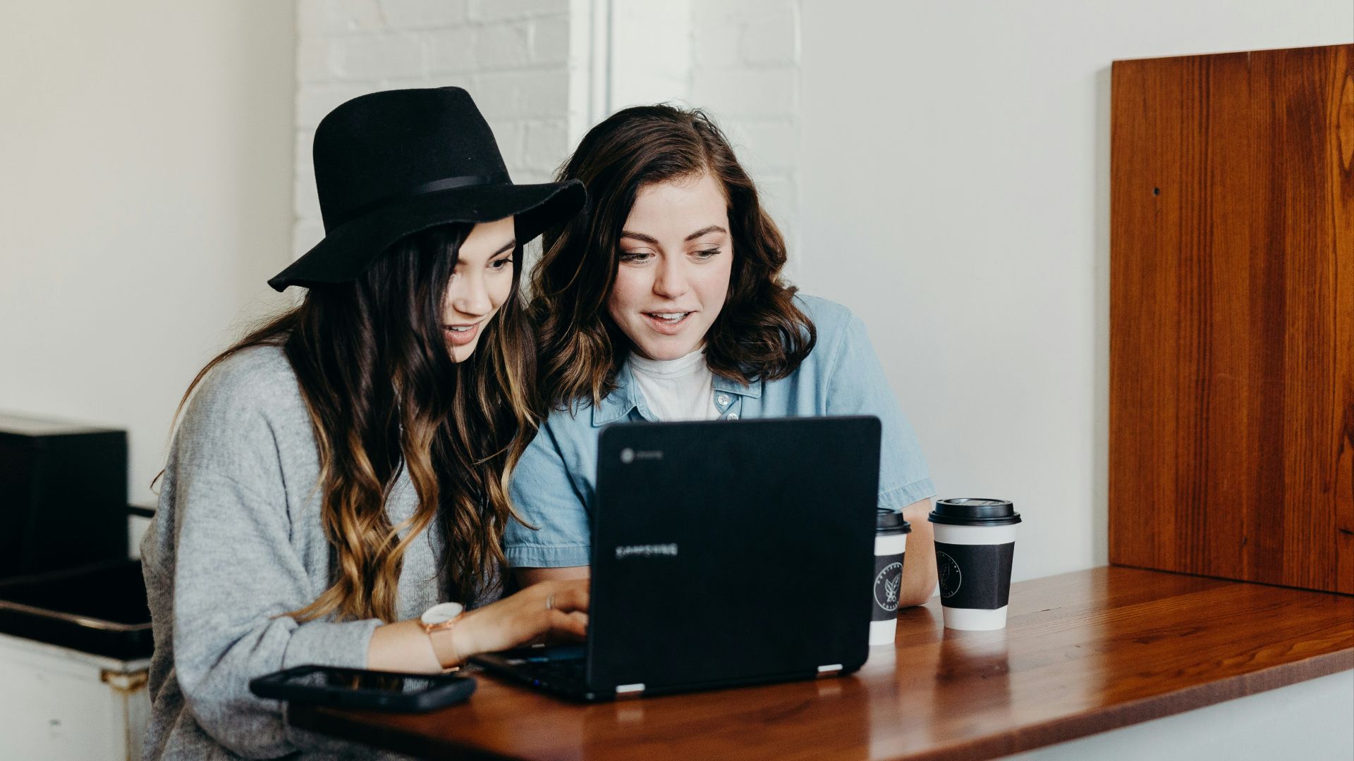 two woman sitting near table using Samsung laptop