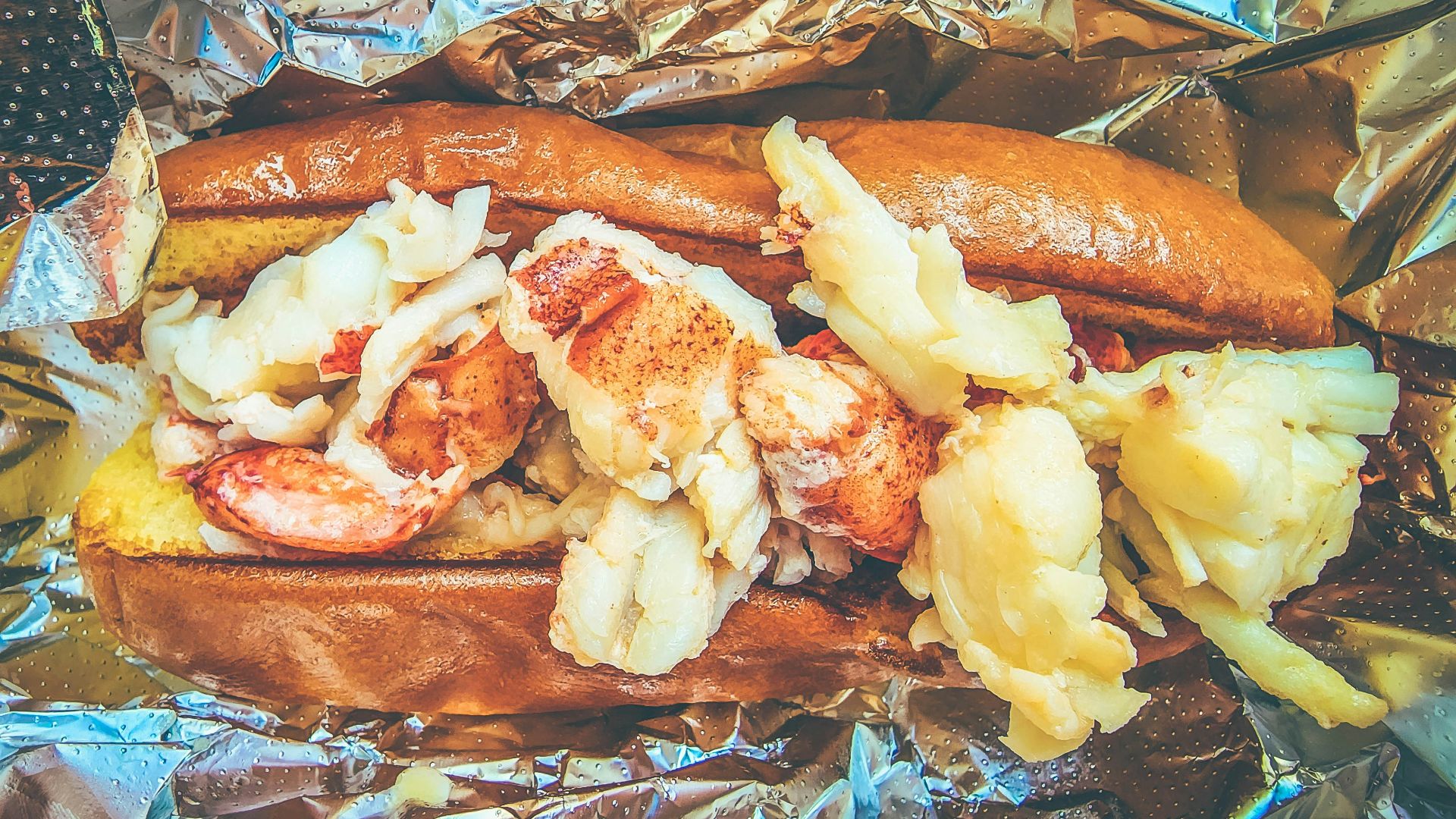 a hot dog with shrimp and potatoes on a piece of tin foil