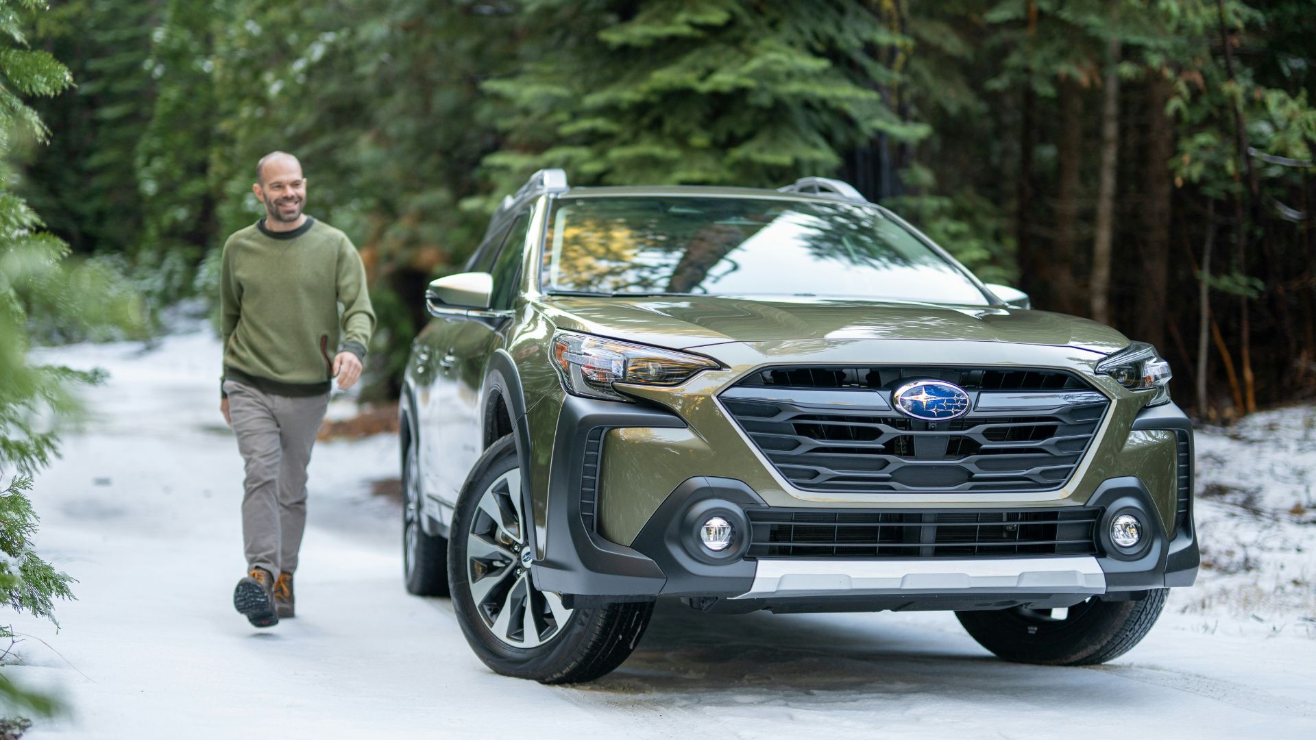 A man walking down a snow covered road next to a car