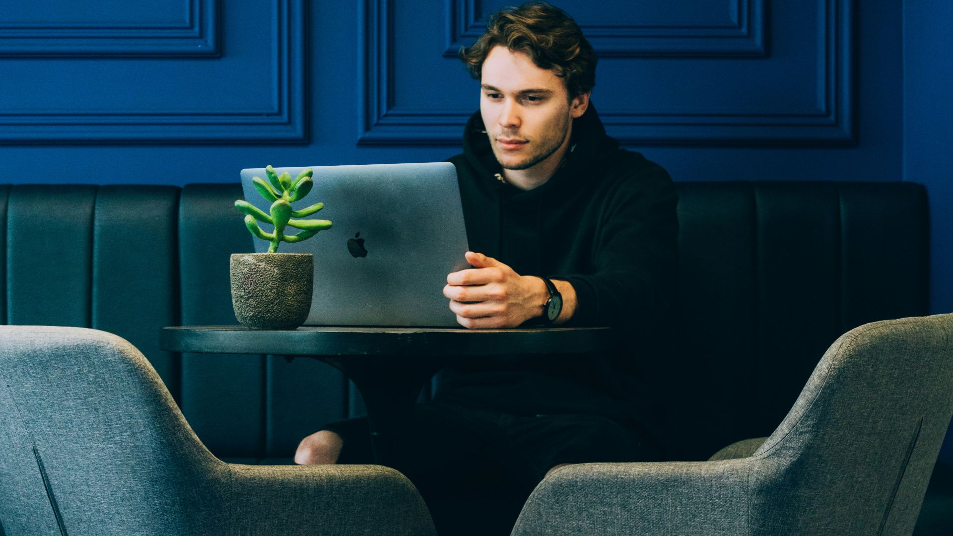 man sitting on couch with looking at his MacBook on table