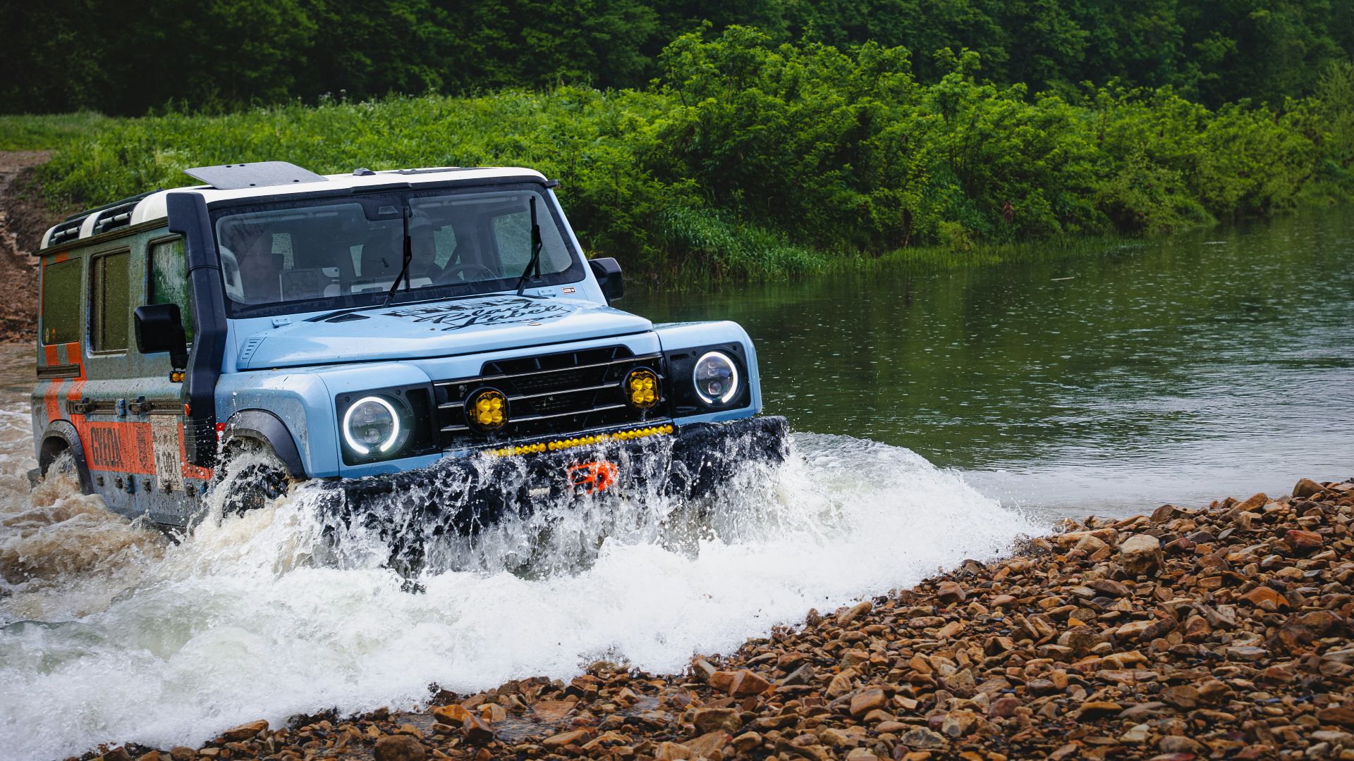 A blue jeep splashes through a river.