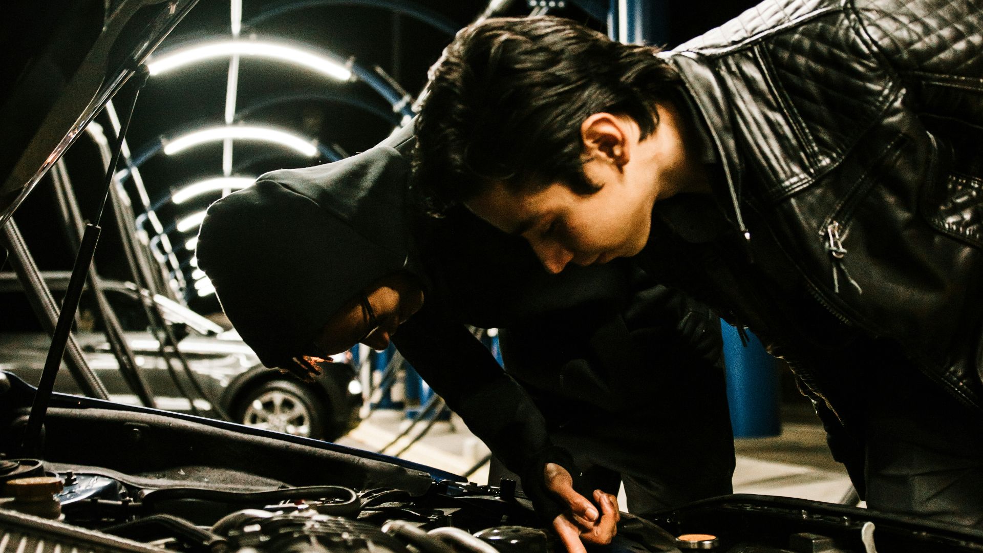 man in black leather jacket and blue denim jeans sitting on black and silver car engine