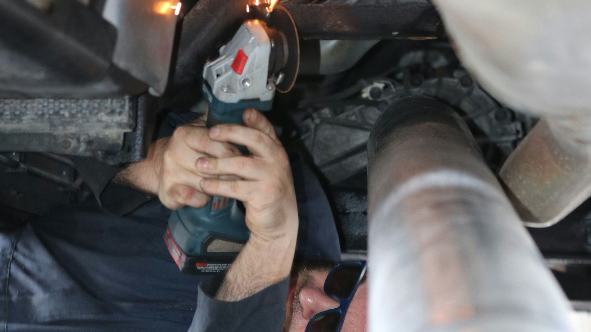 A mechanic uses a grinder under a car.