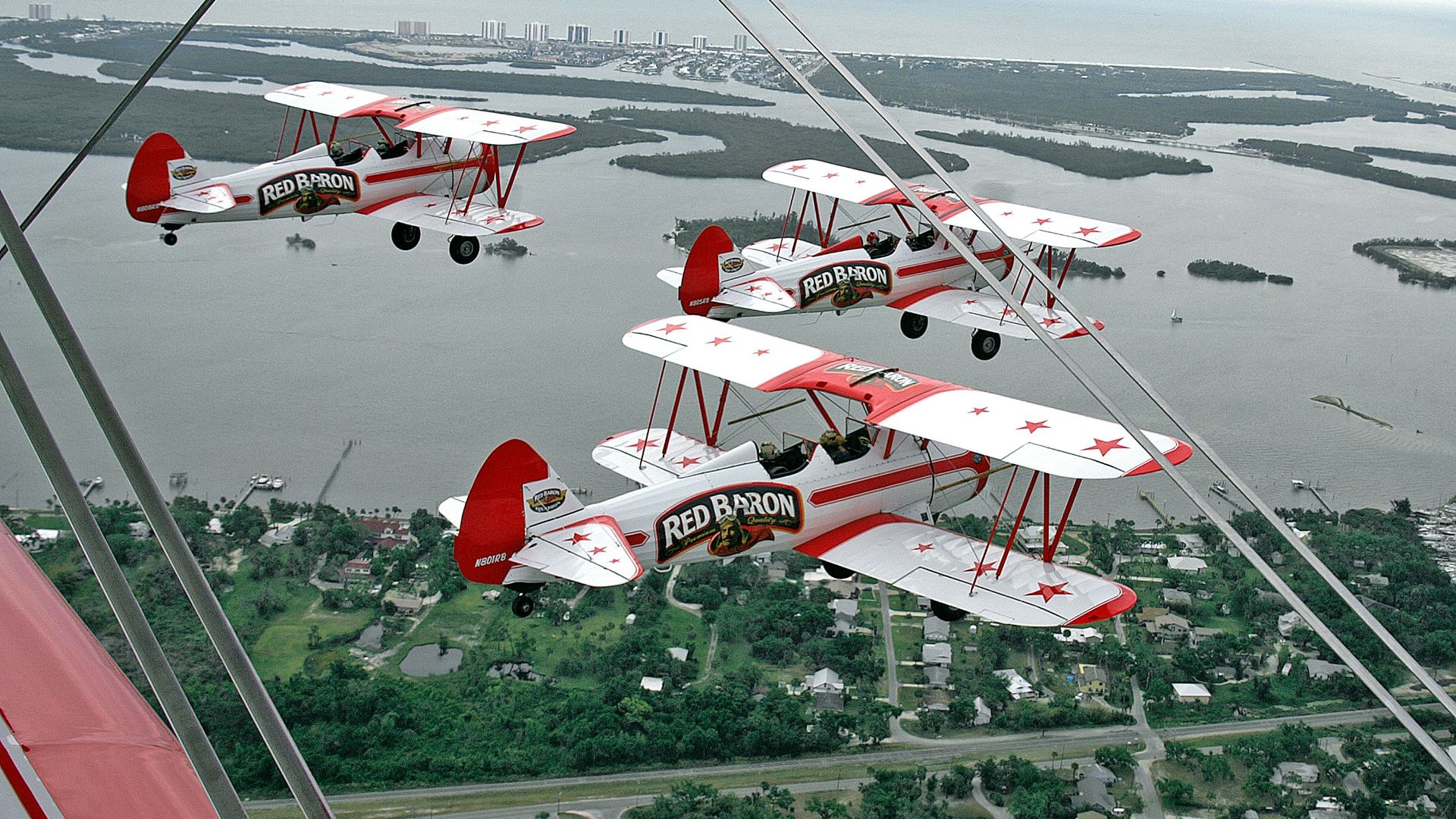 Four biplanes fly in formation over a coastal landscape.