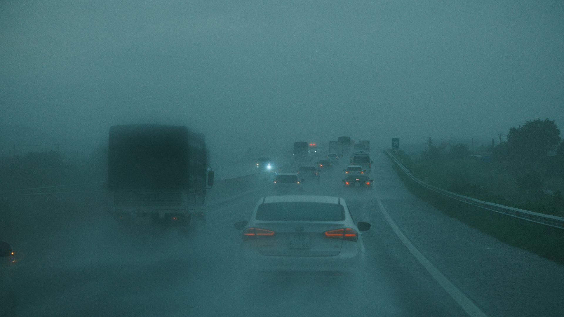 Cars driving on a wet highway in heavy fog.