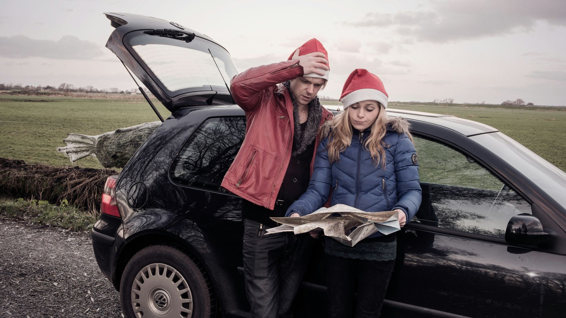 a man and woman standing in front of a car with a large fish in the trunk
