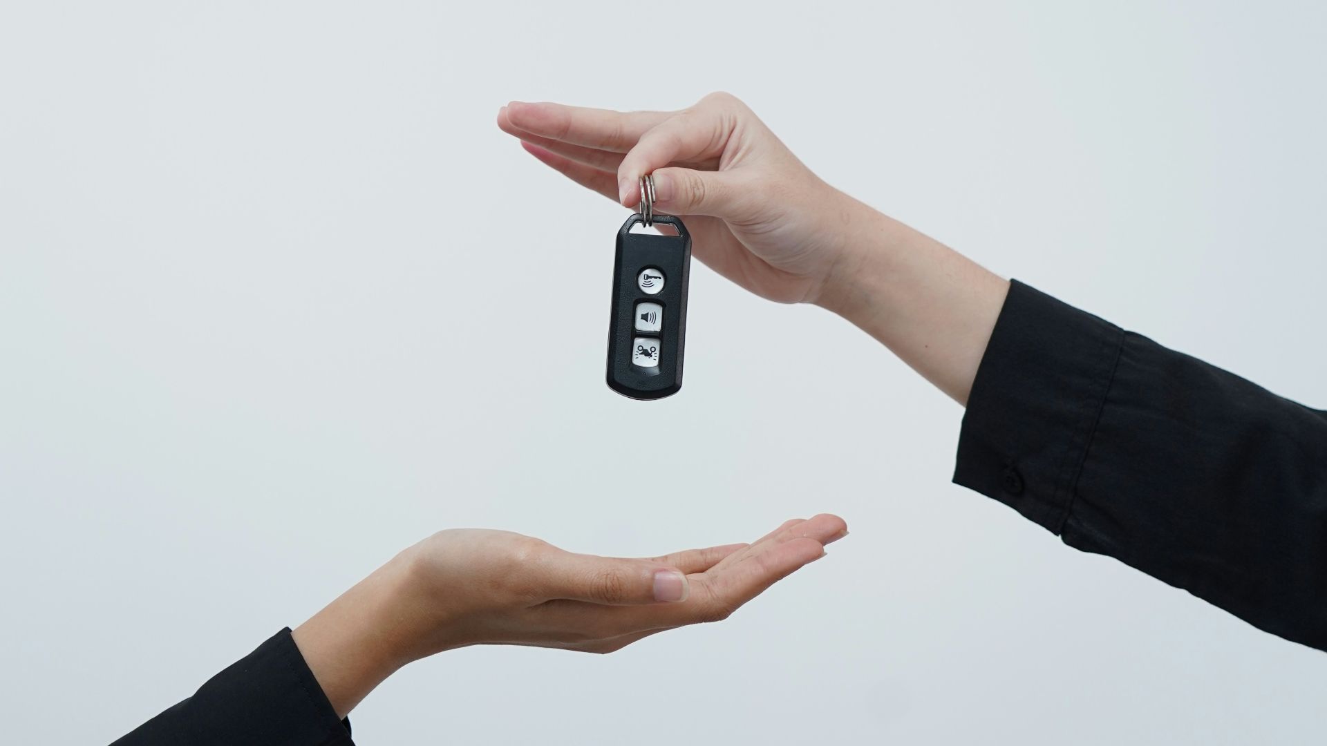 Hands exchanging a car key against a light background