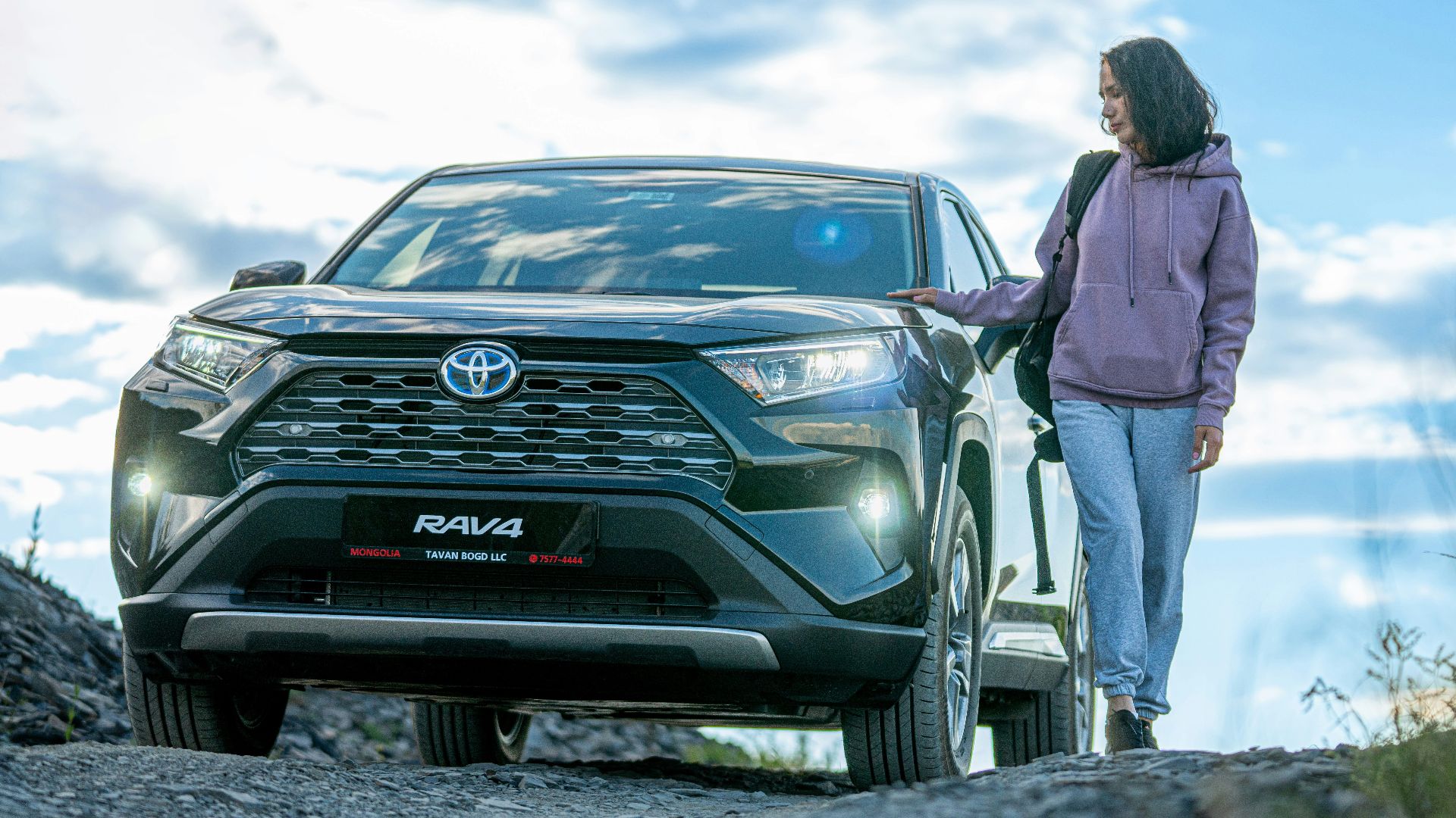 A woman standing next to a car on a dirt road