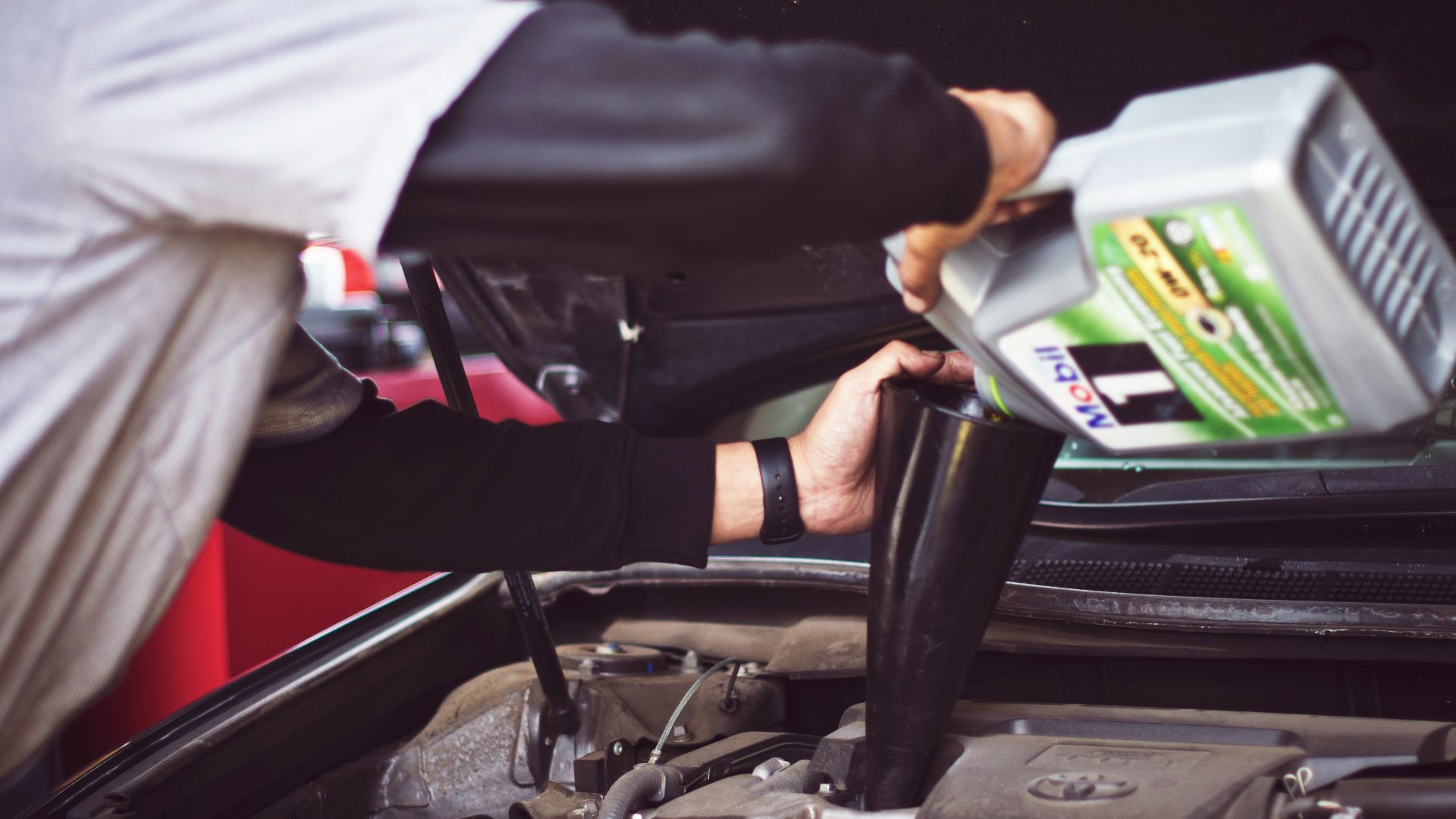man refilling motor oil on car engine bay