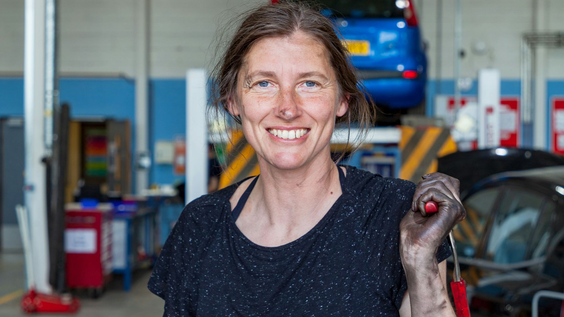 a woman holding a wrench in a garage