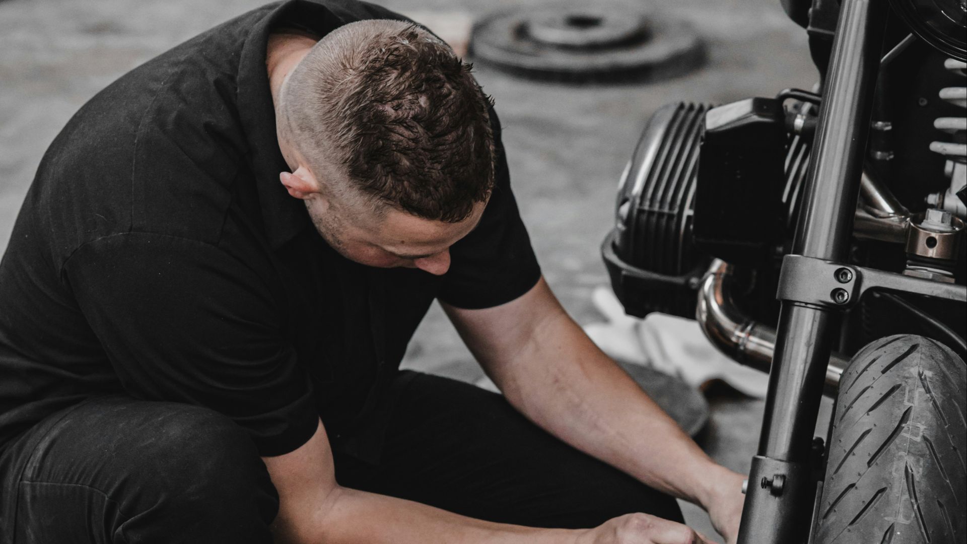 man in black t-shirt and black pants sitting on black motorcycle tire