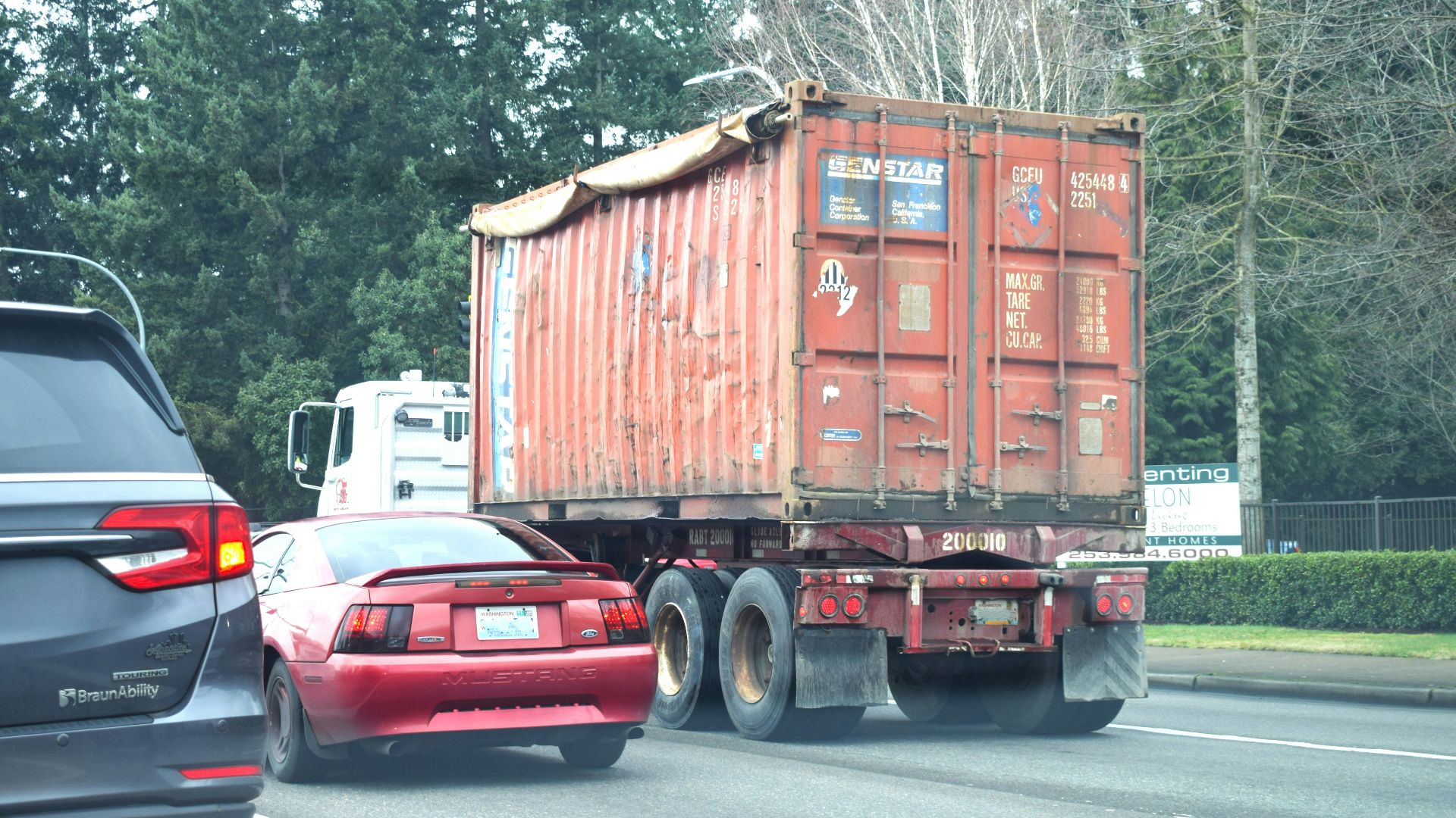 a red truck driving down a street next to a forest