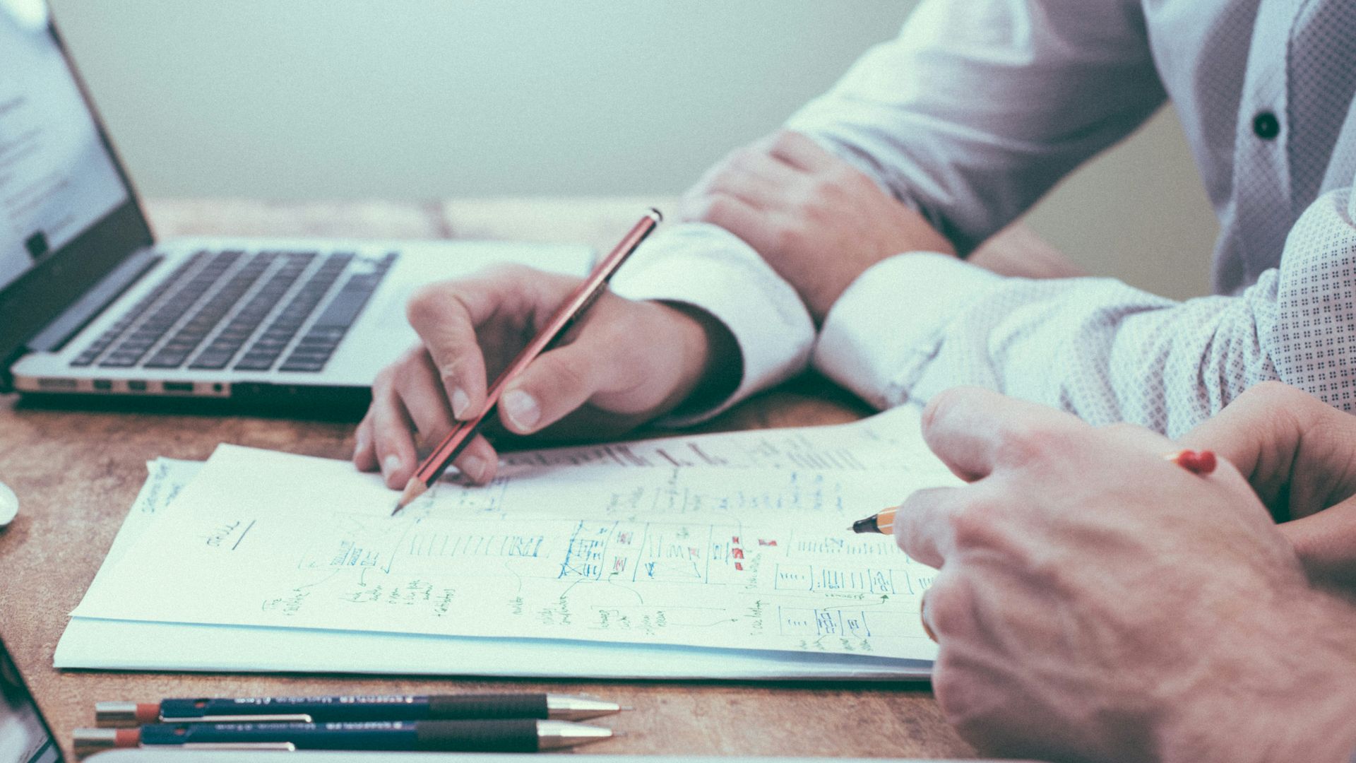 person holding pencil near laptop computer