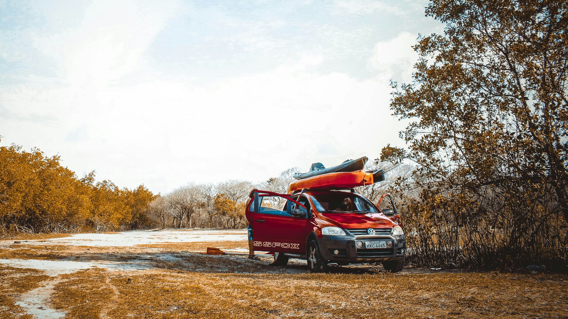 red vehicle on dirt road near trees at daytime