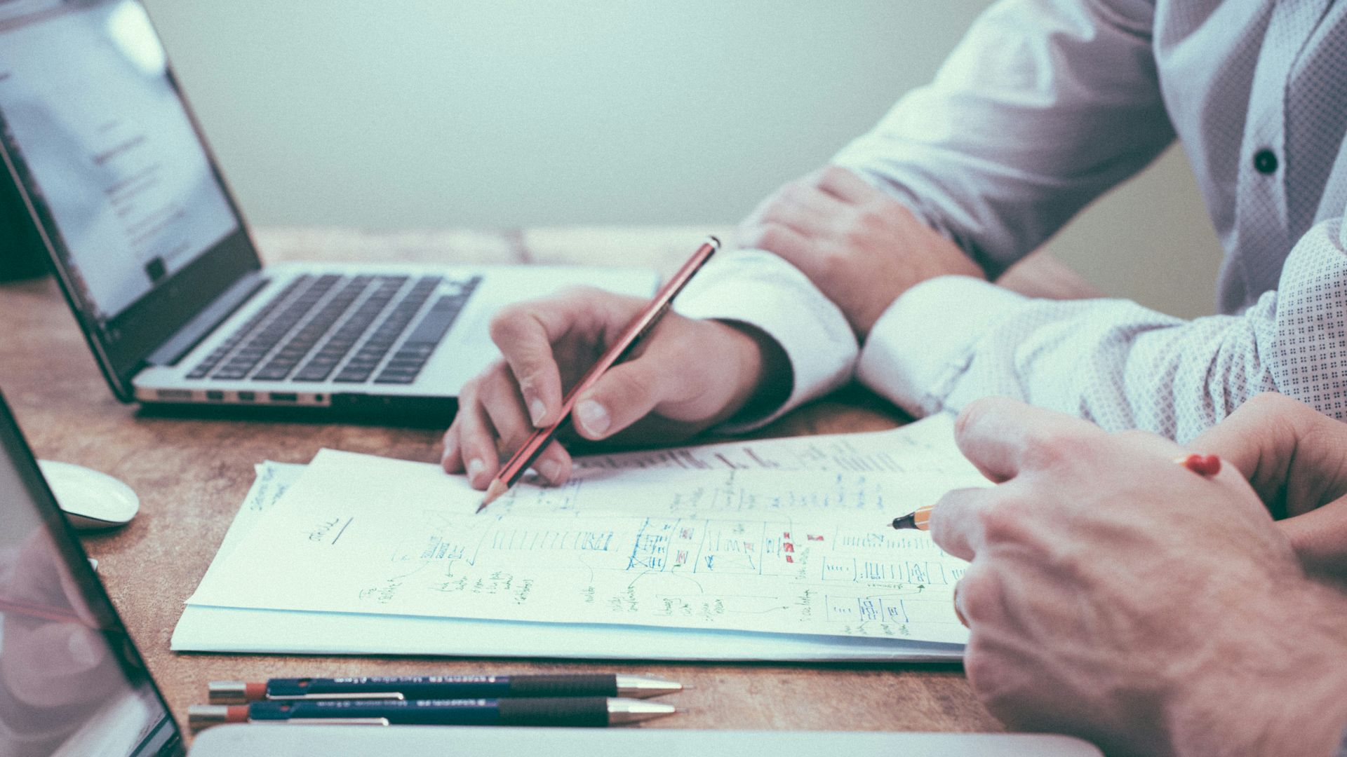 person holding pencil near laptop computer