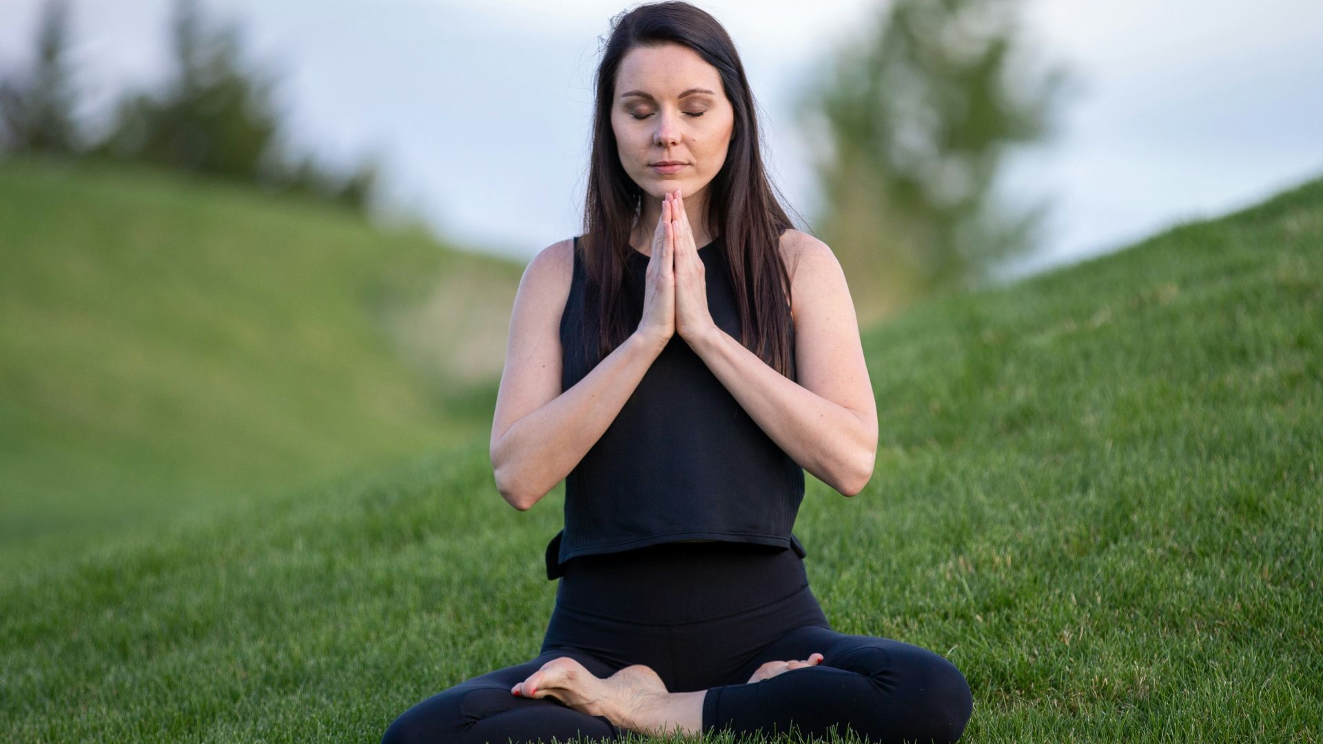 woman in black tank top and black pants sitting on green grass field during daytime