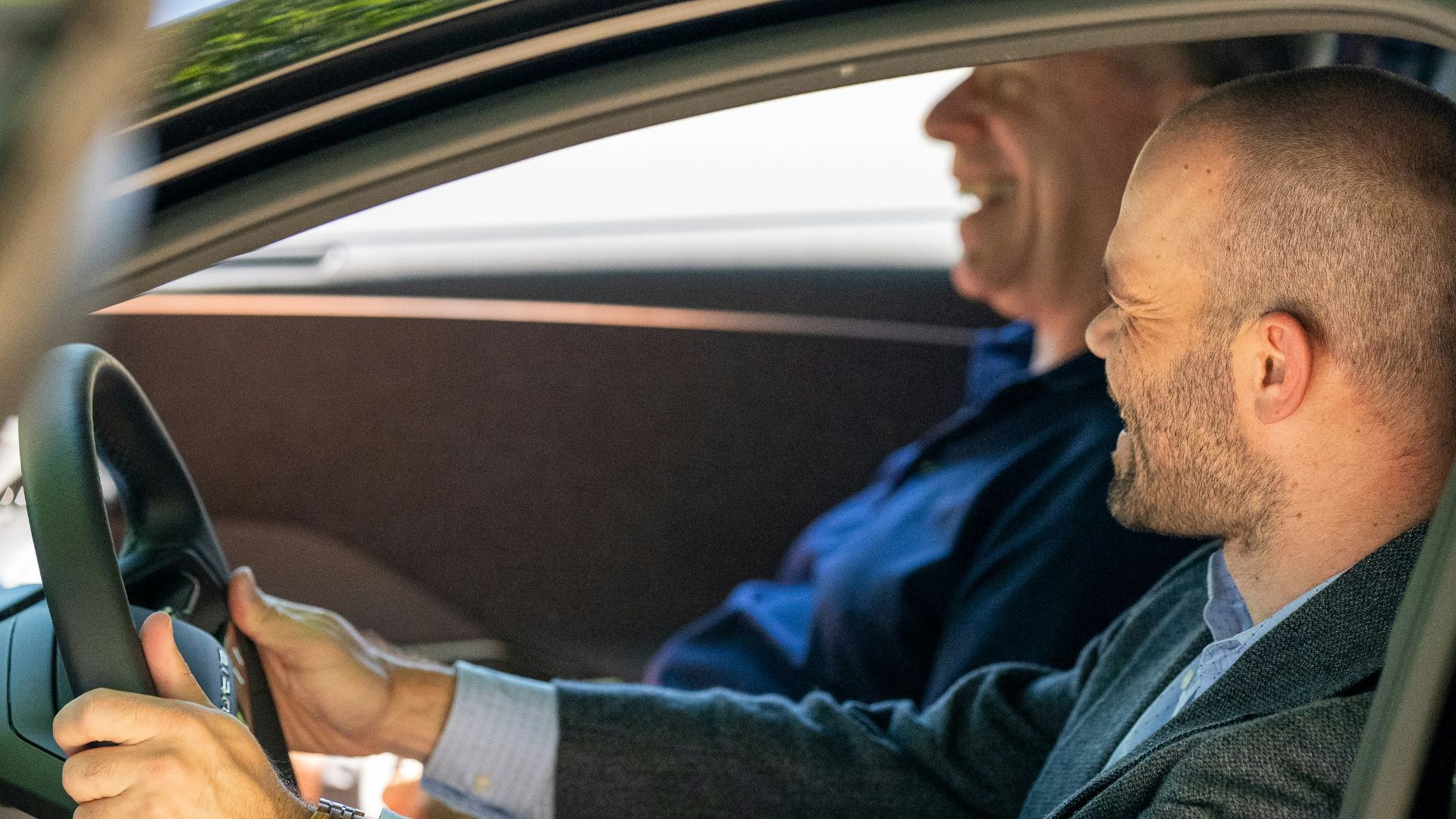 a man driving a car with another man behind him
