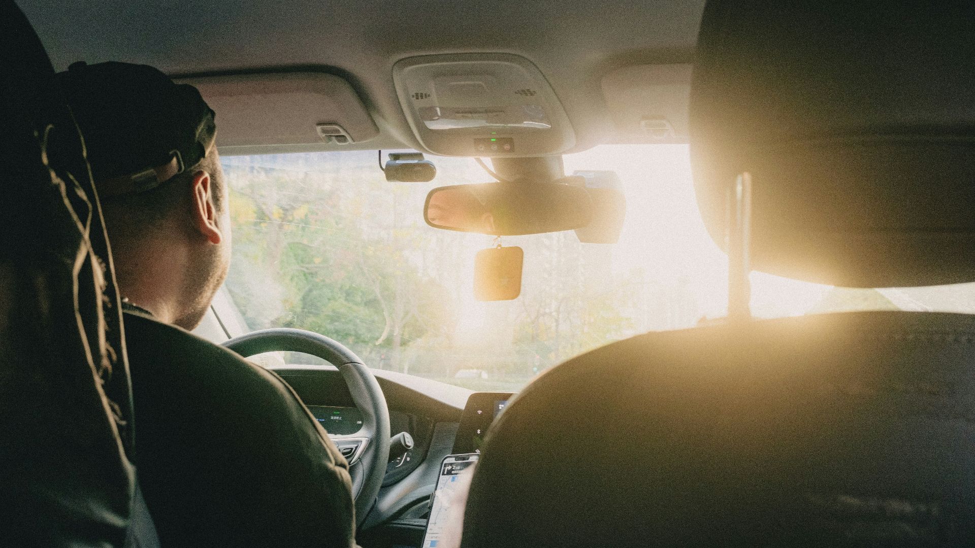 a man driving a car with the sun shining through the windshield