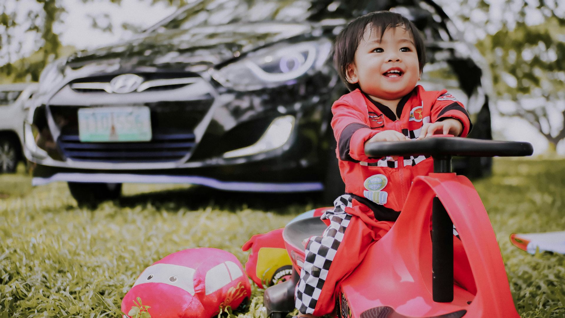 boy riding wiggle car on grass near sedan