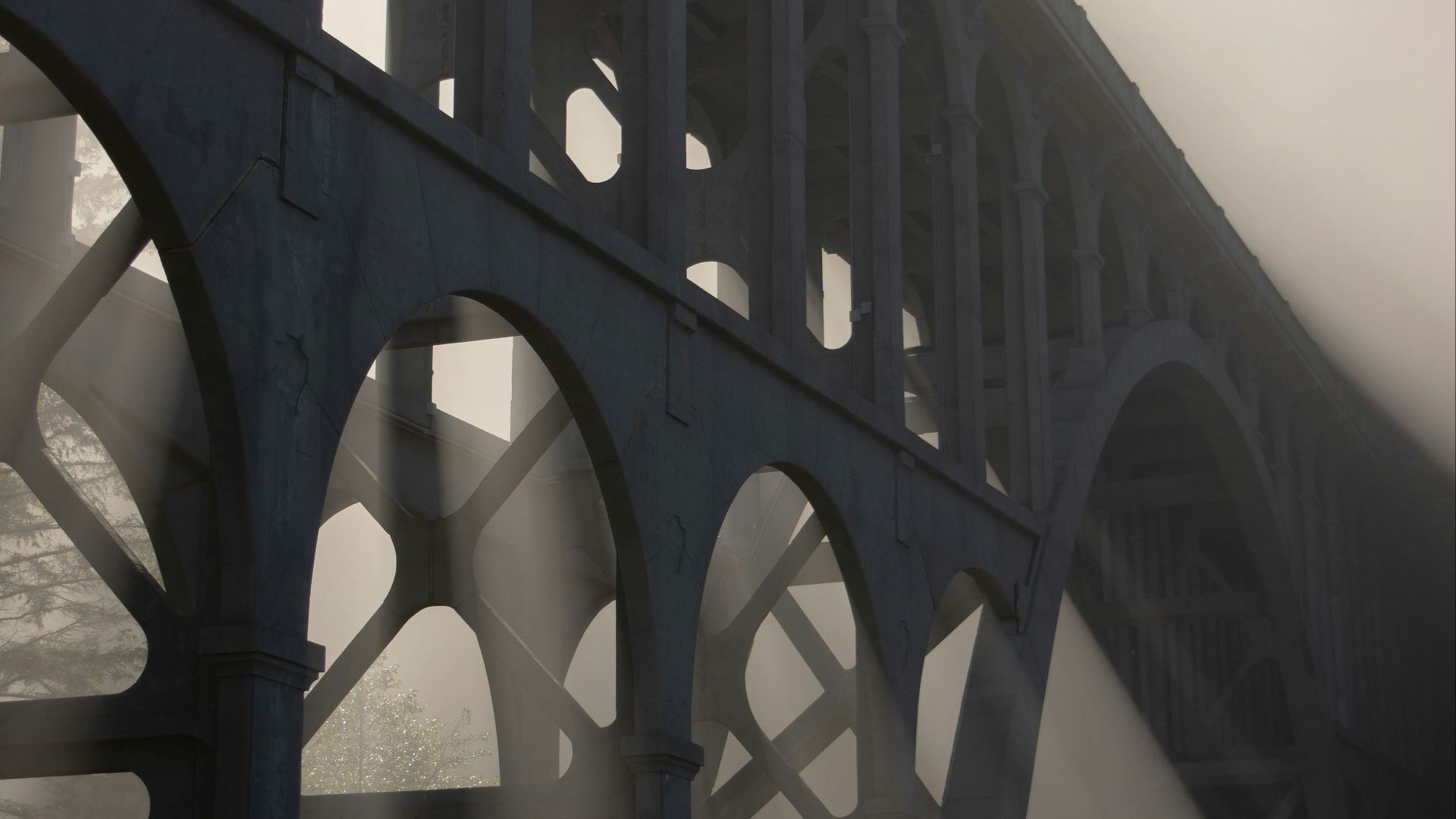 a foggy bridge with sunlight coming through the arches