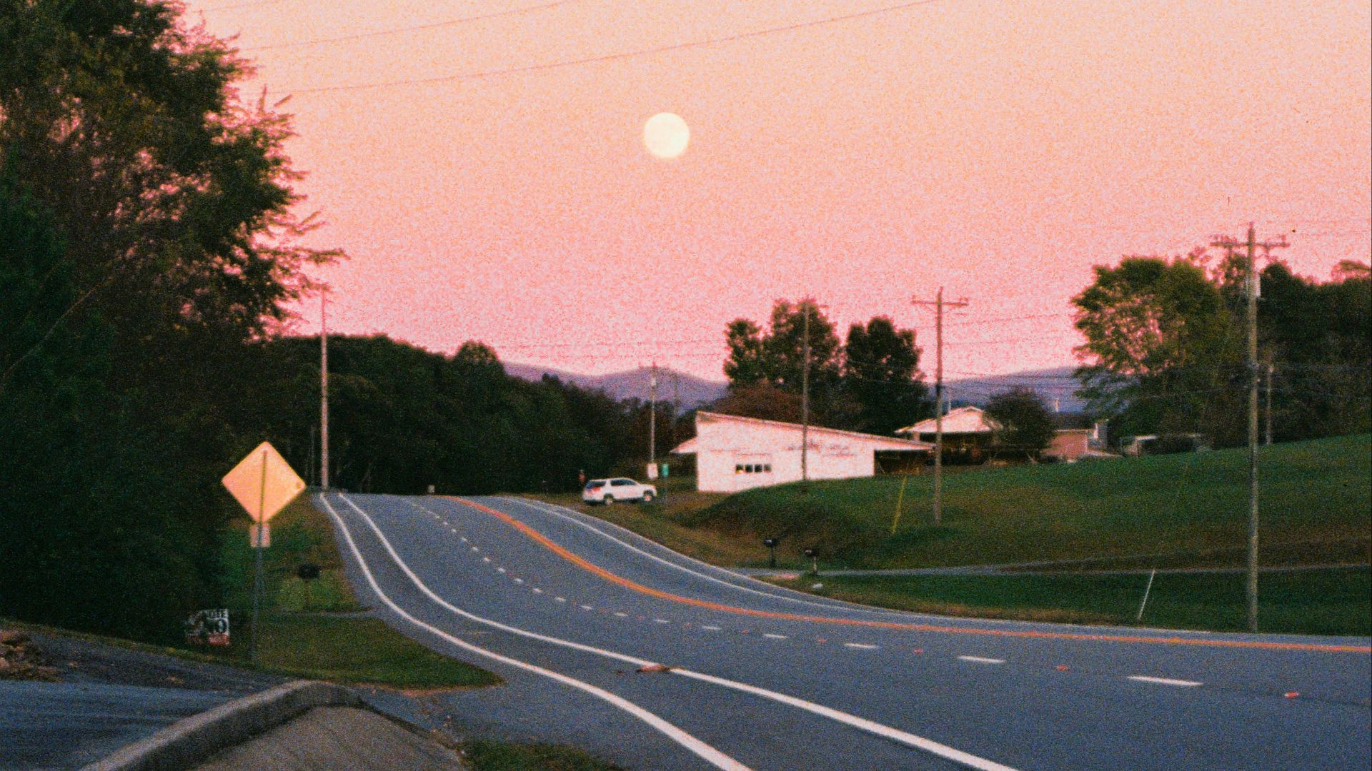 A road leads toward the moon in a pink sky.