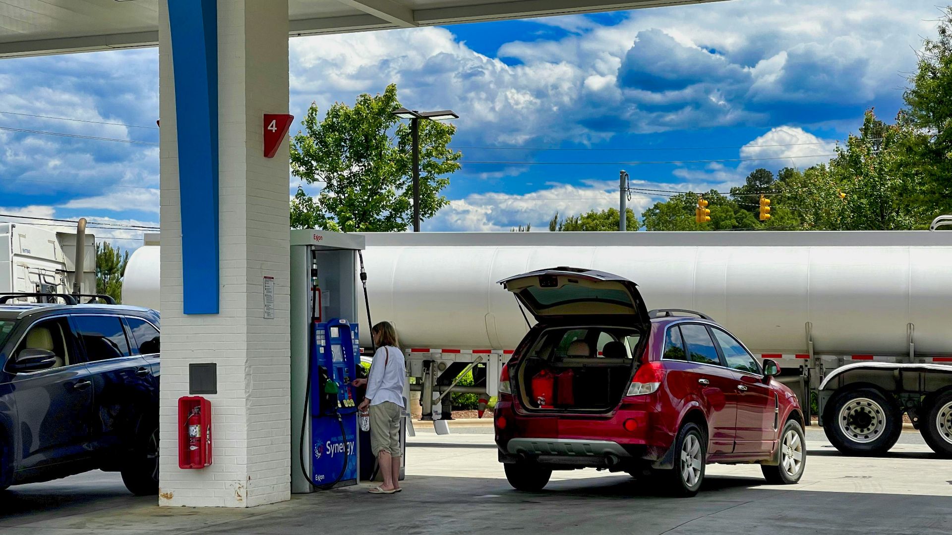 man in white t-shirt standing beside red suv during daytime