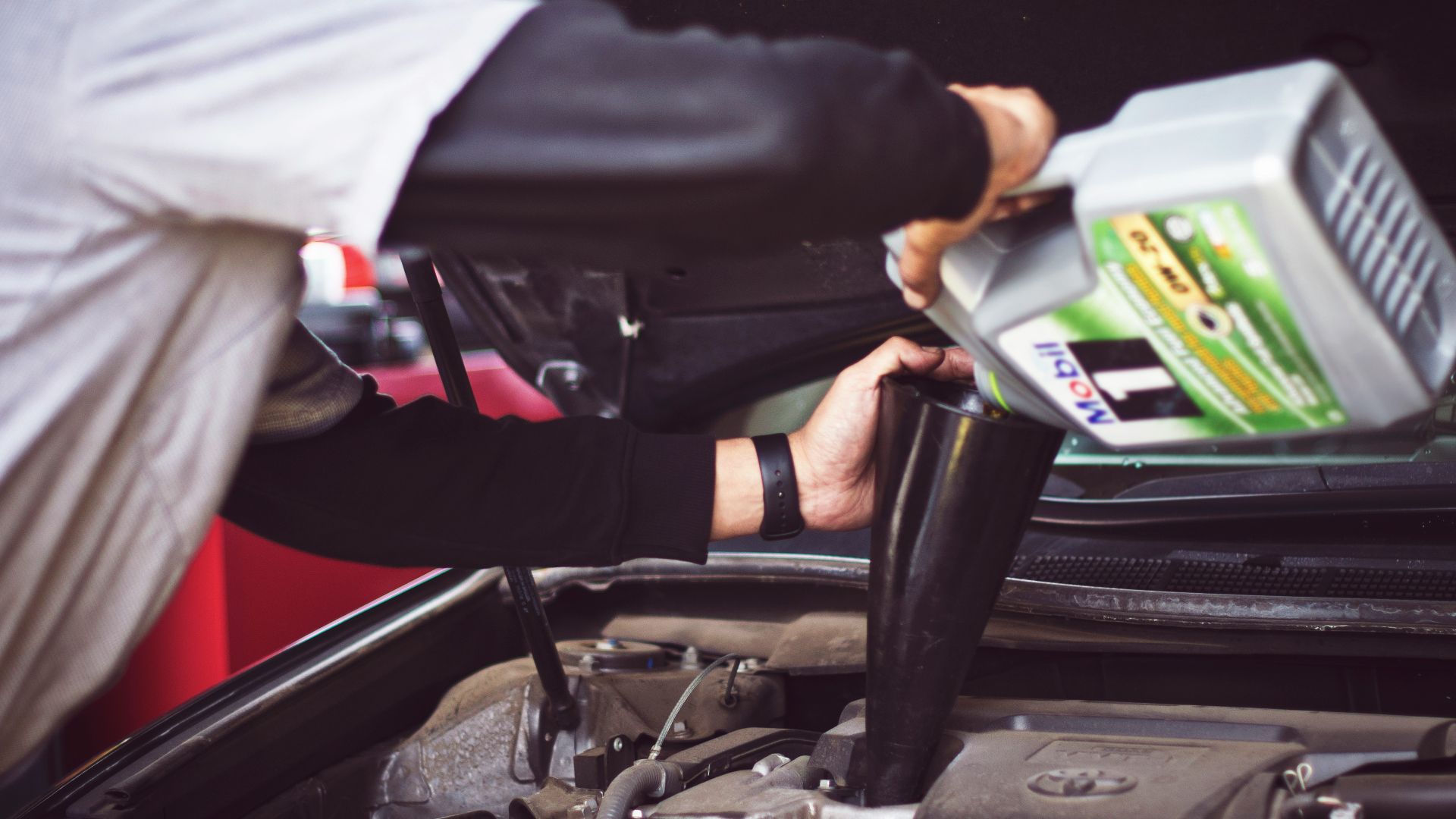 man refilling motor oil on car engine bay