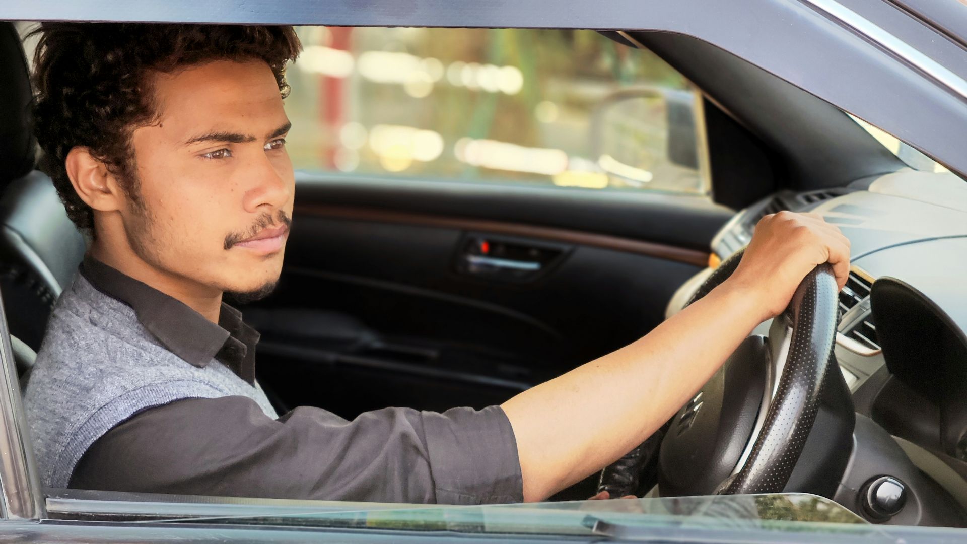 A young man drives a car on a sunny day.