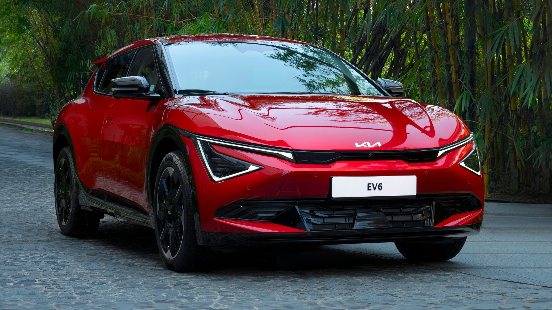 A red car driving down a street next to trees