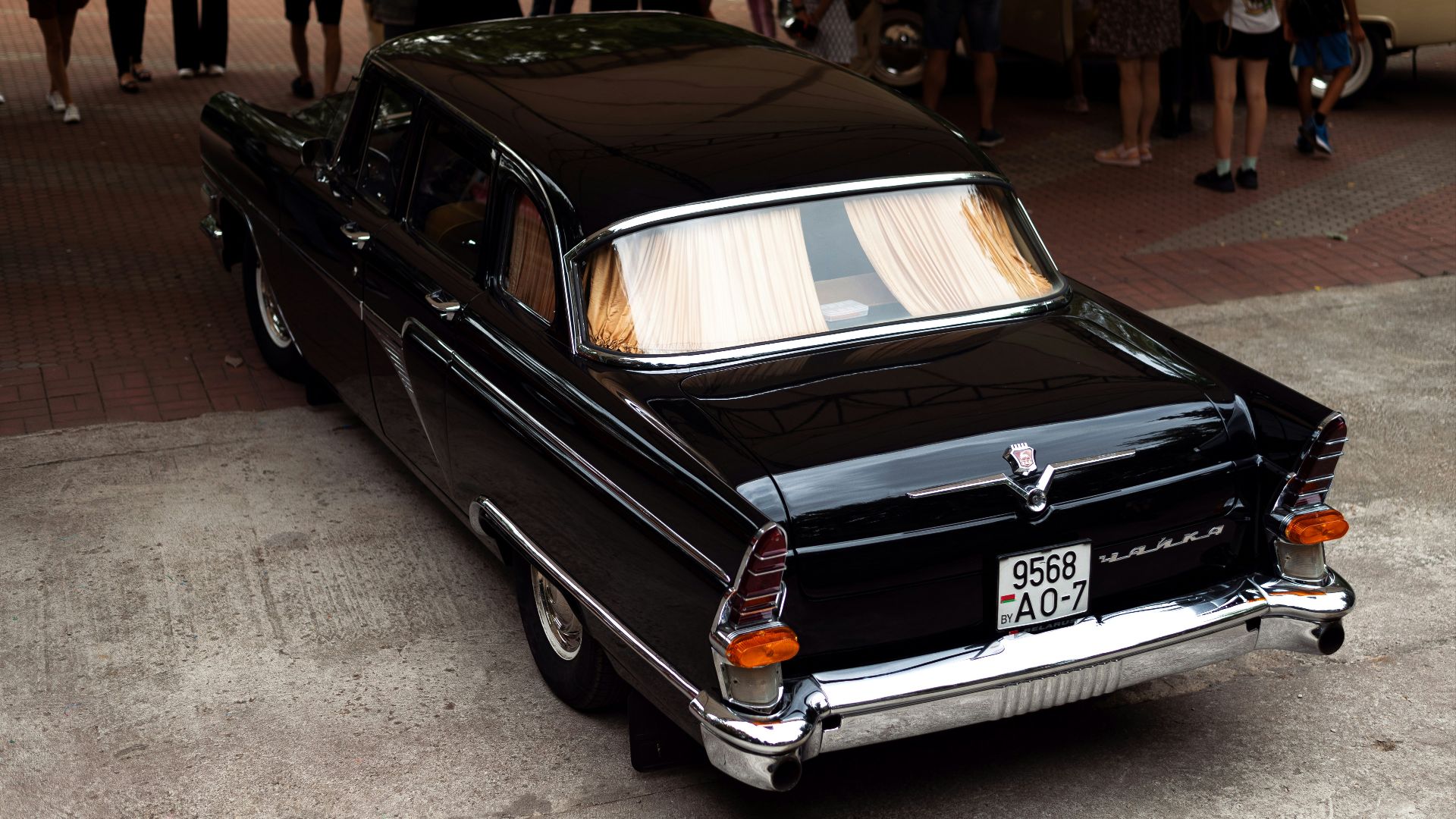 a black car parked on a brick road with people walking around