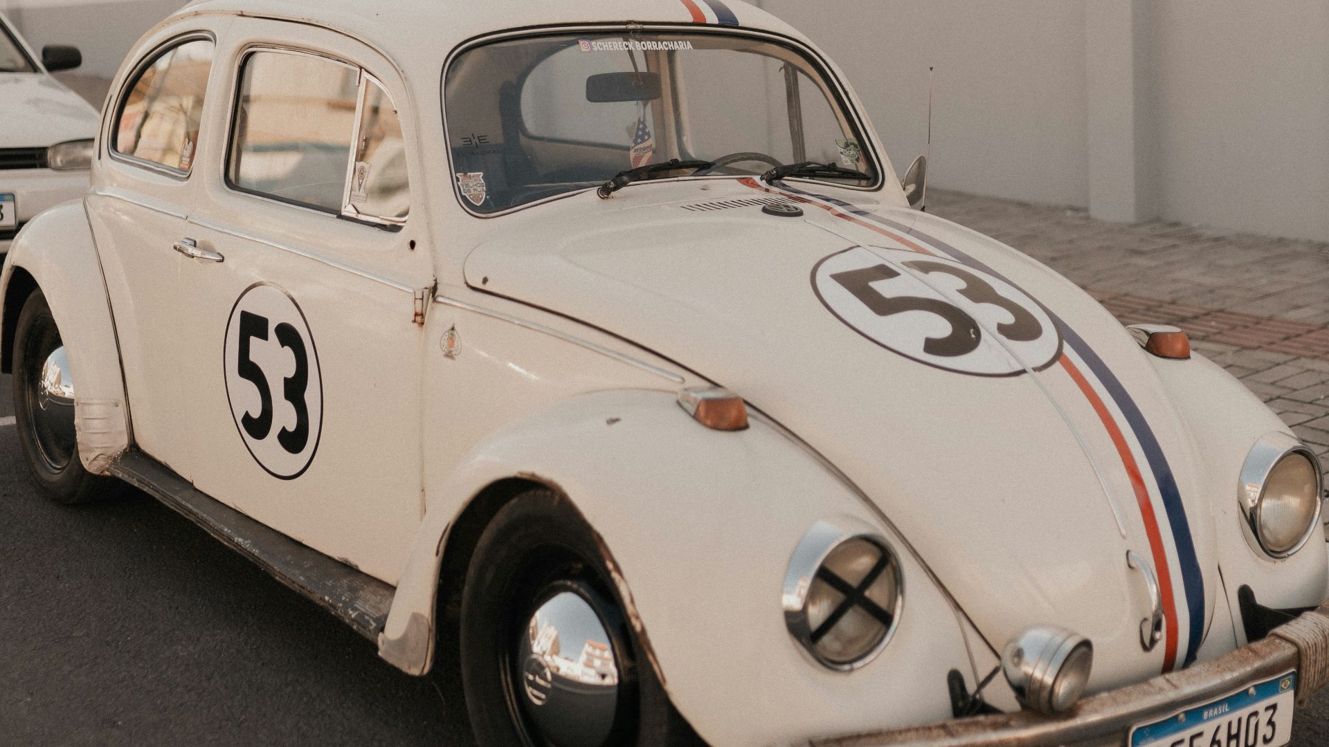 A white vw bug driving down a street next to a white building