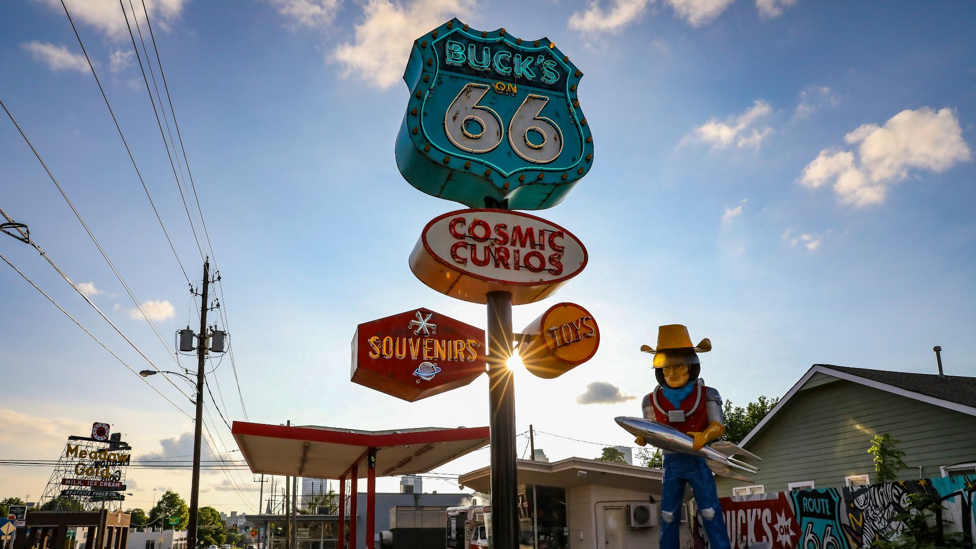 a statue of a cowboy holding a surfboard in front of a gas station