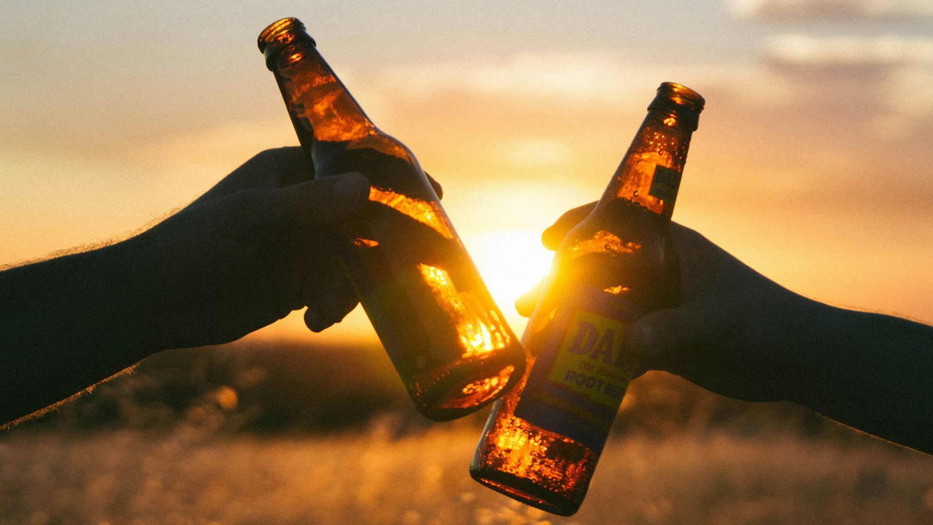 photography of person holding glass bottles during sunset