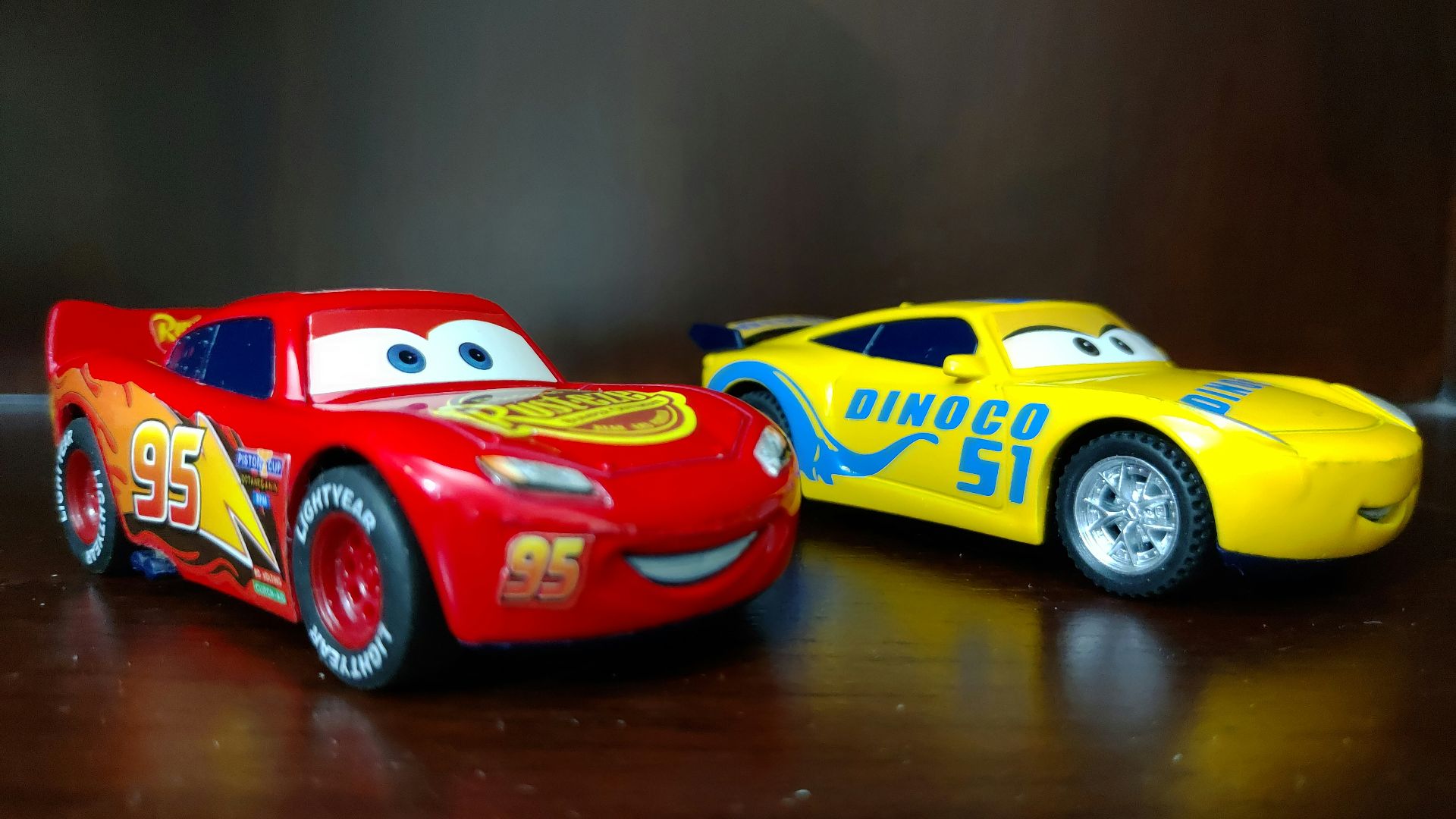 two red and yellow Disney Cars plastic toys on brown wooden surface