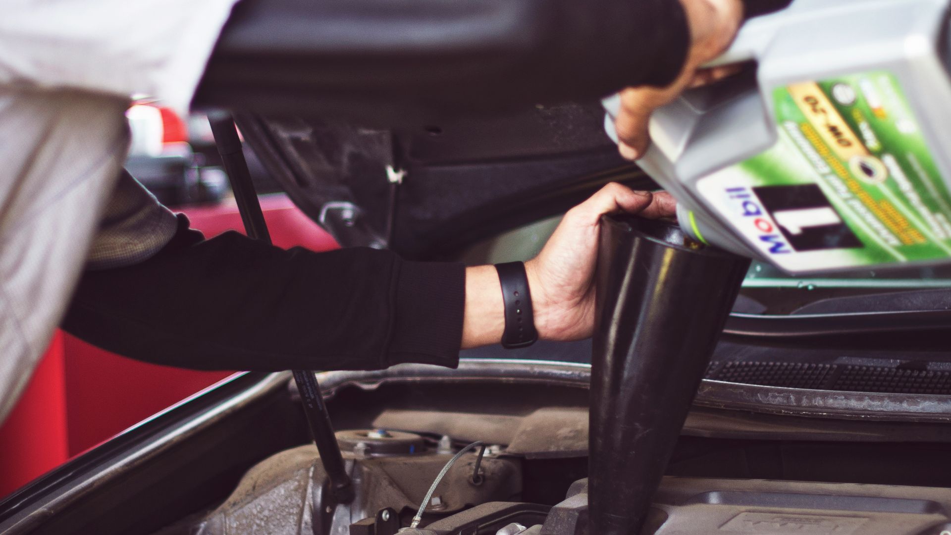 man refilling motor oil on car engine bay
