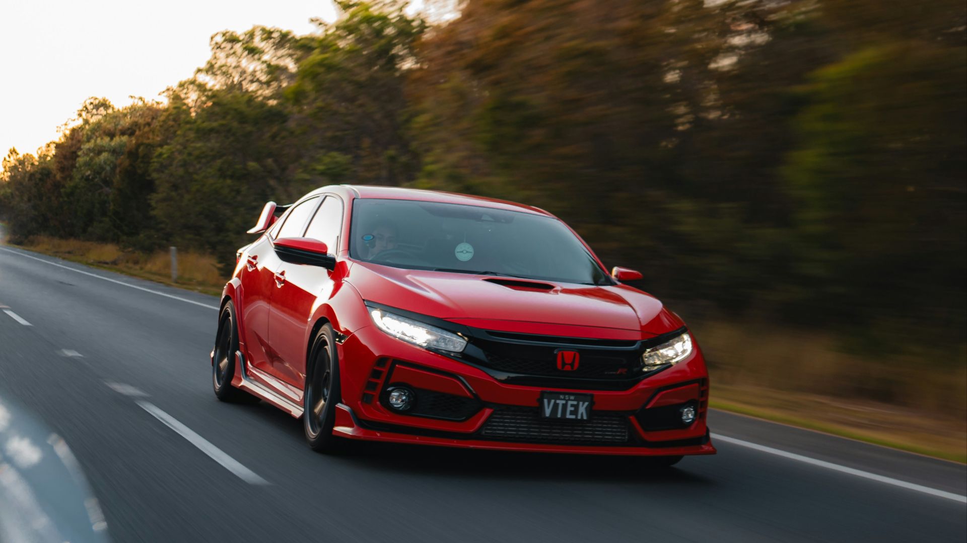 a red car driving down a road next to trees