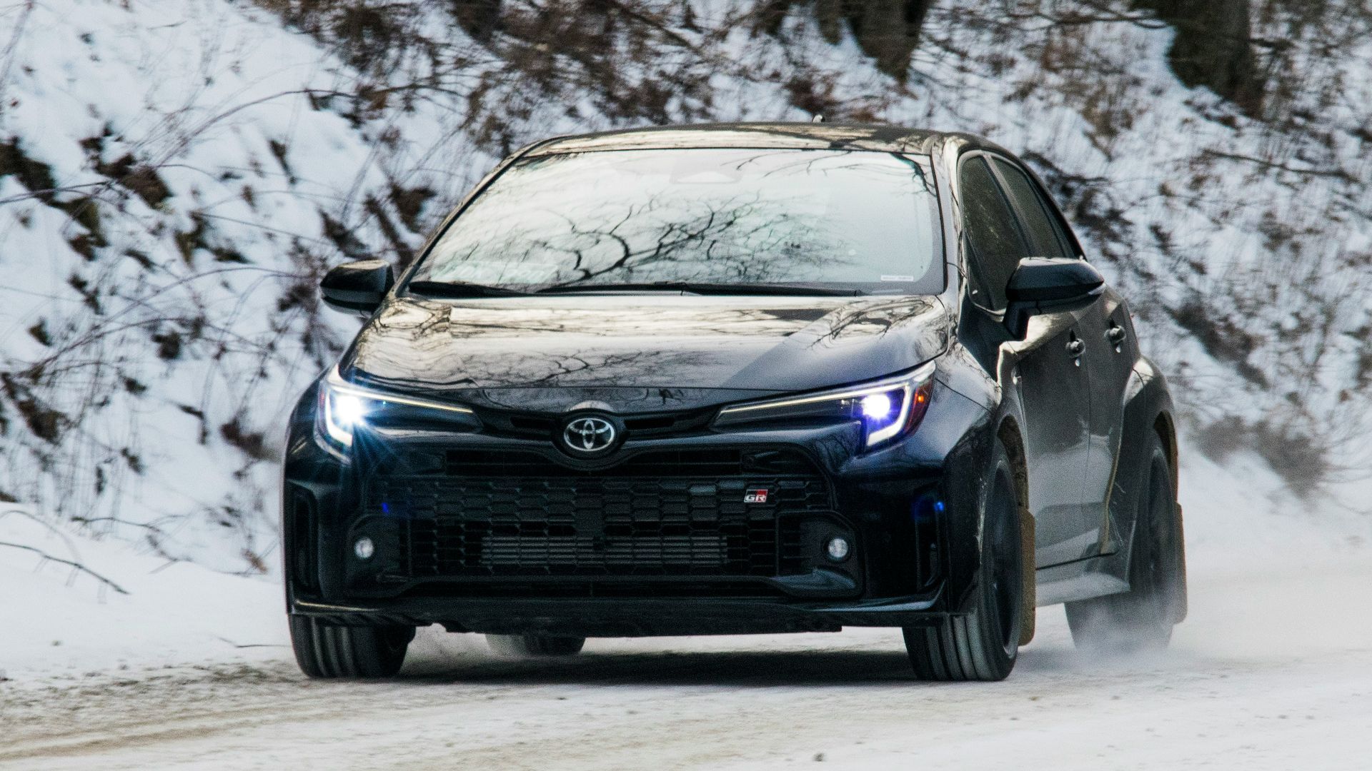 A black car drives through snowy conditions.