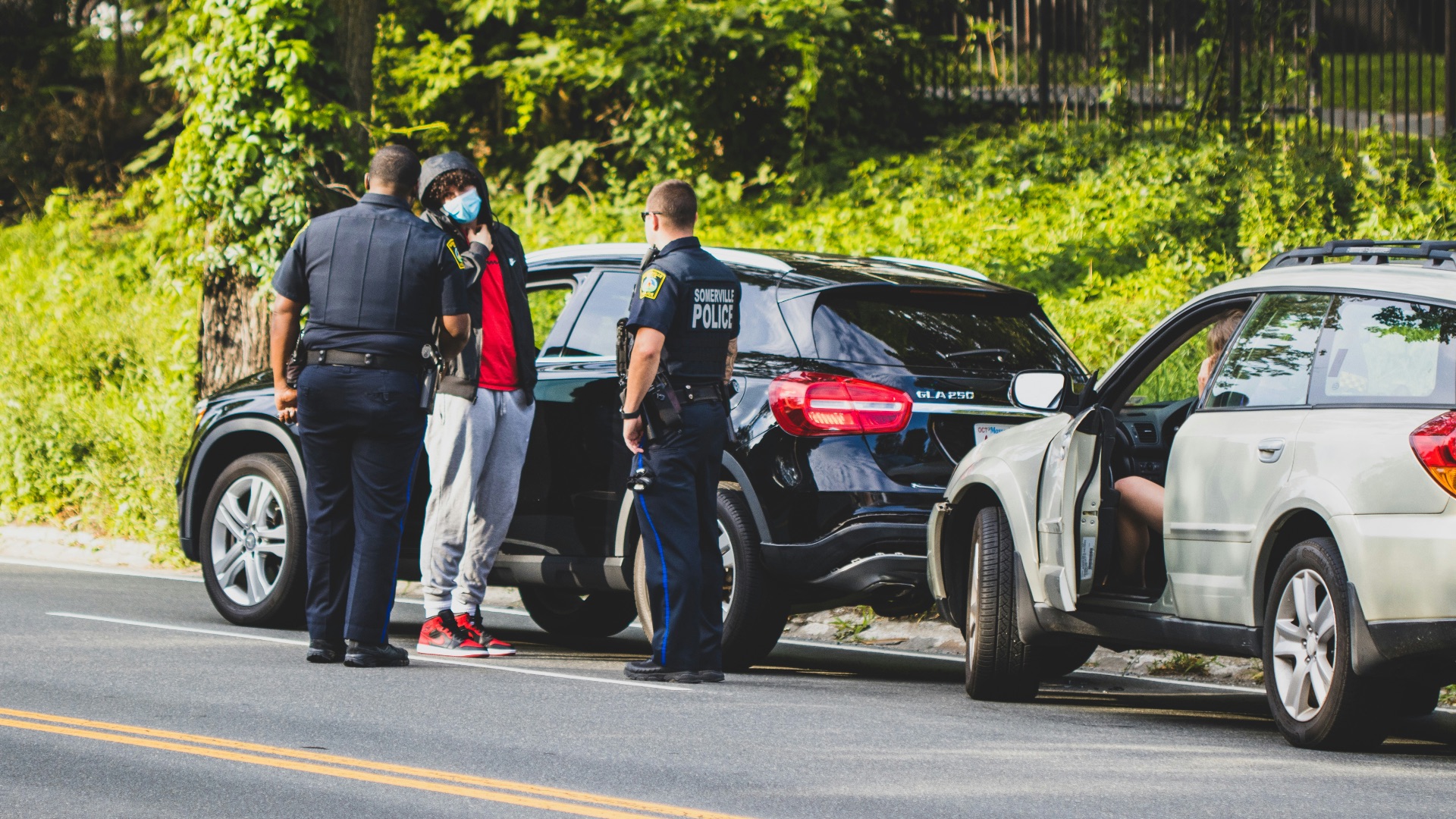 man in black t-shirt and black pants standing beside black suv during daytime