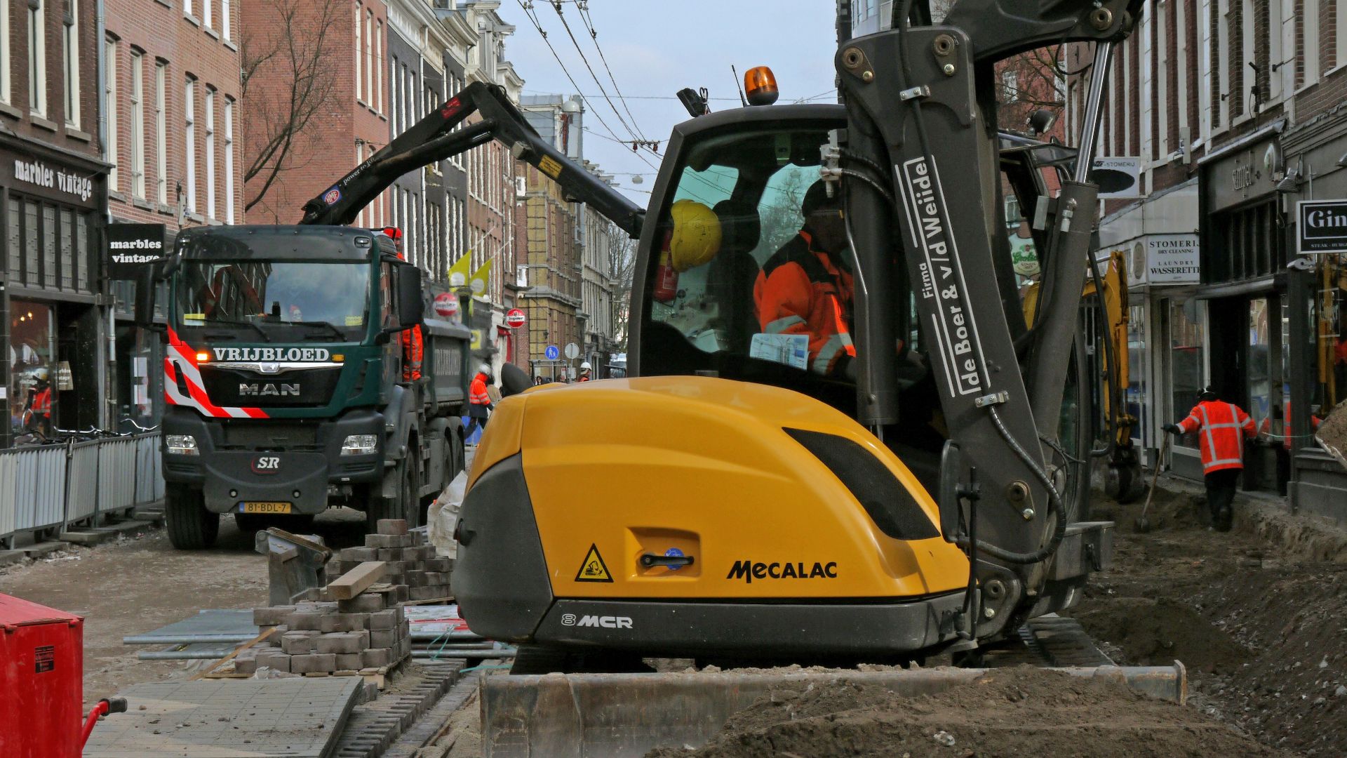 person using heavy equipment near vehicles, people, and buildings