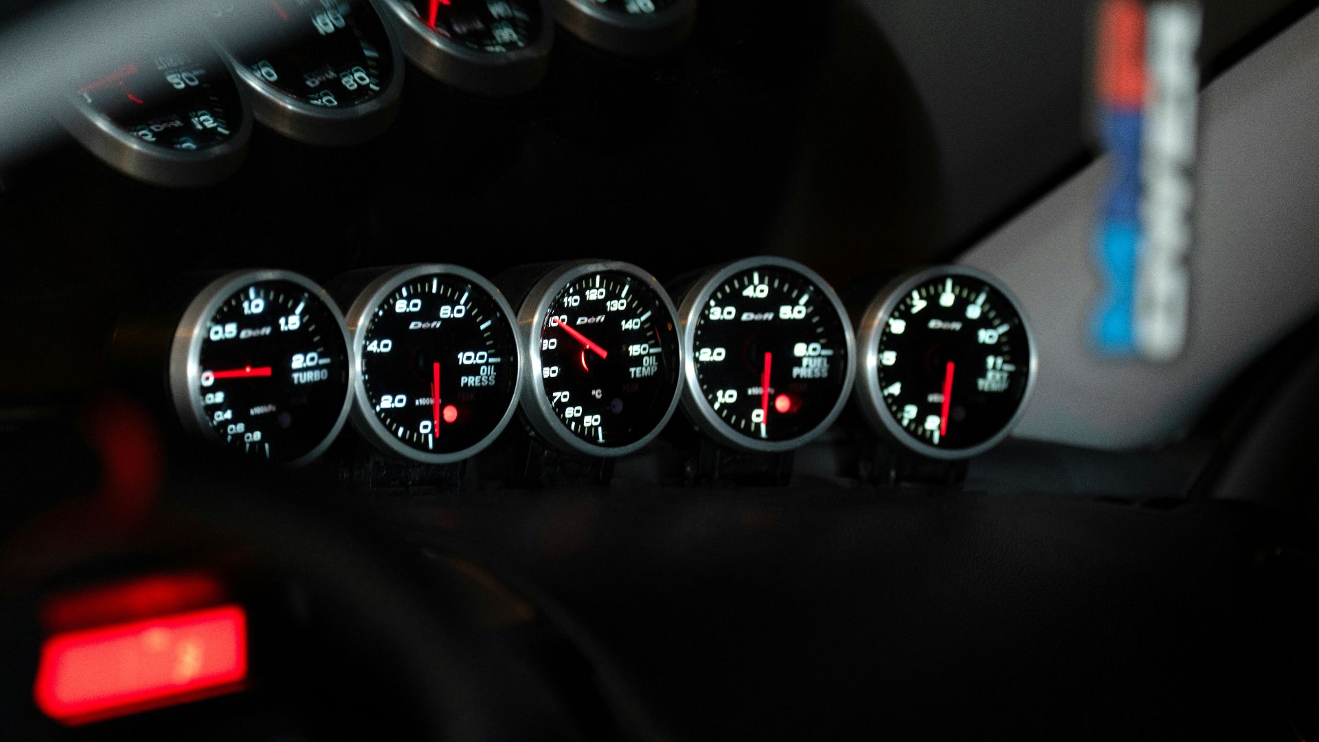 Five car dashboard gauges illuminated at night.