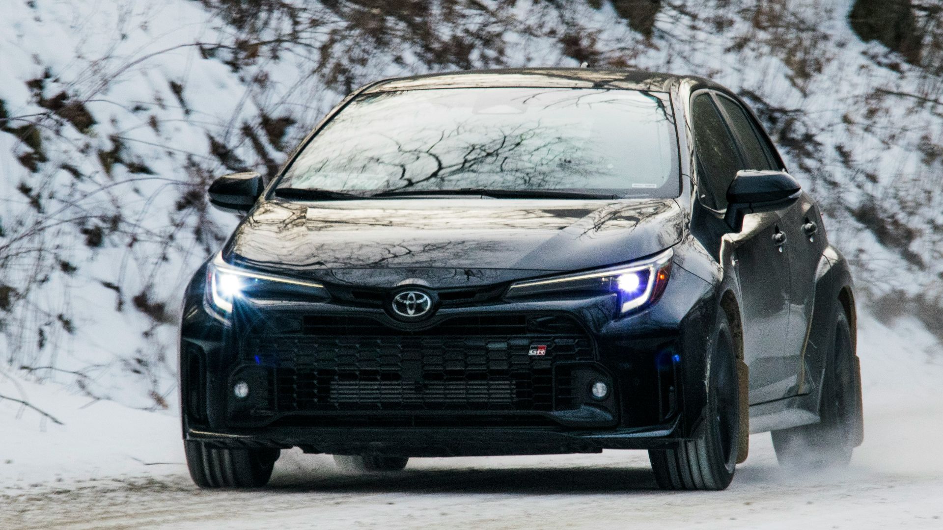 A black car drives through snowy conditions.
