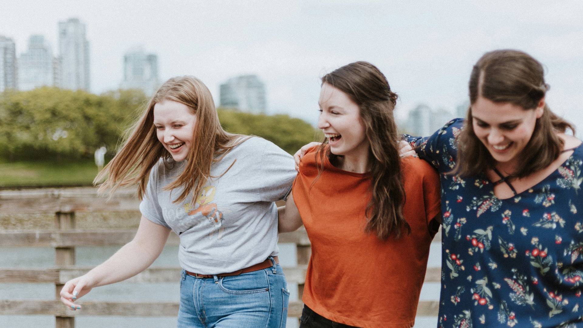three women walking on brown wooden dock near high rise building during daytime